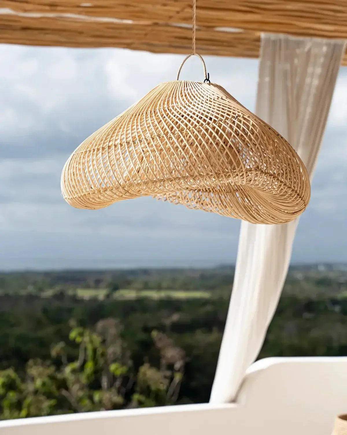 Woven pendant light hanging from a thatched roof with a scenic background