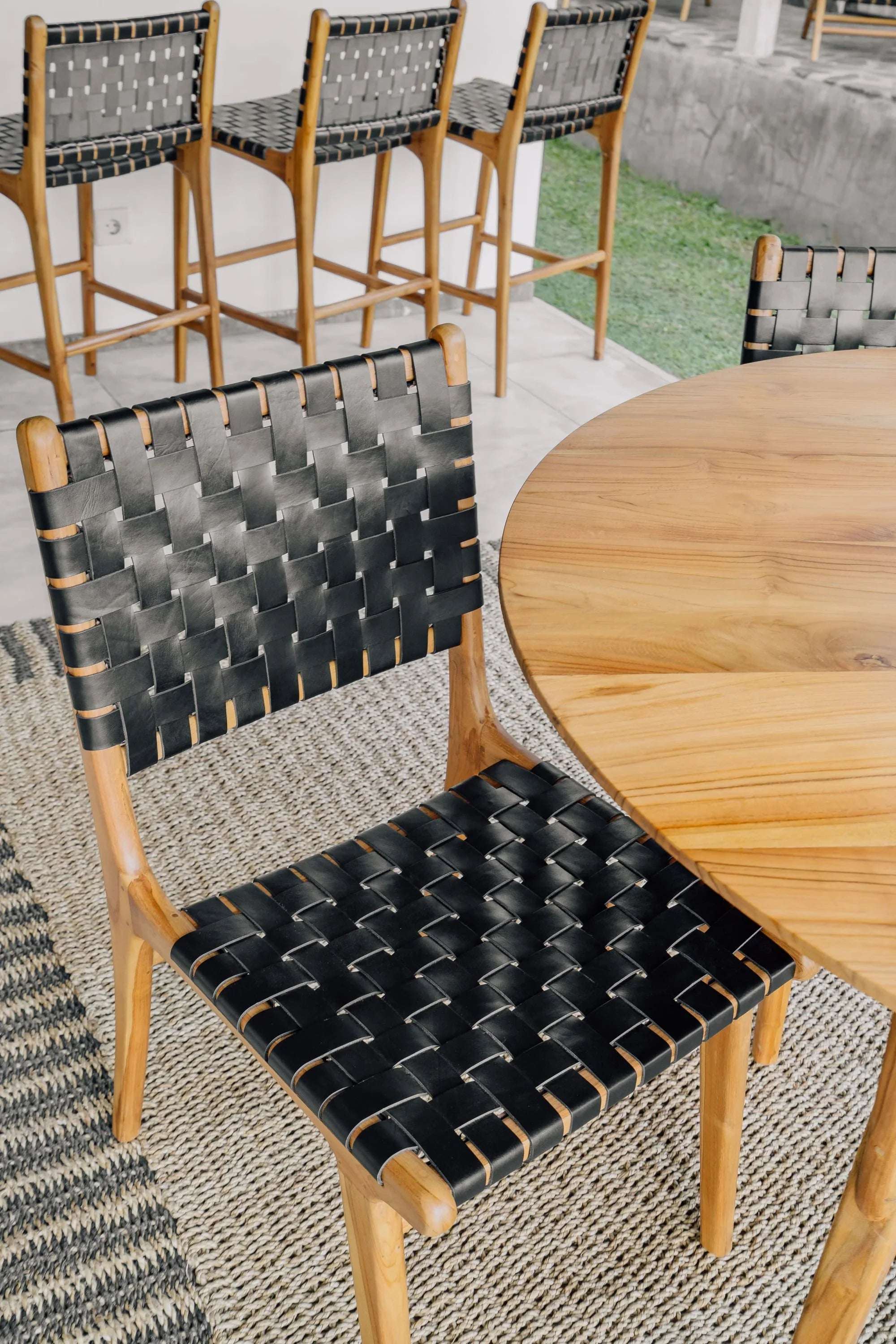 Handmade wooden dining chair with black woven seat and back, next to a round wood table.