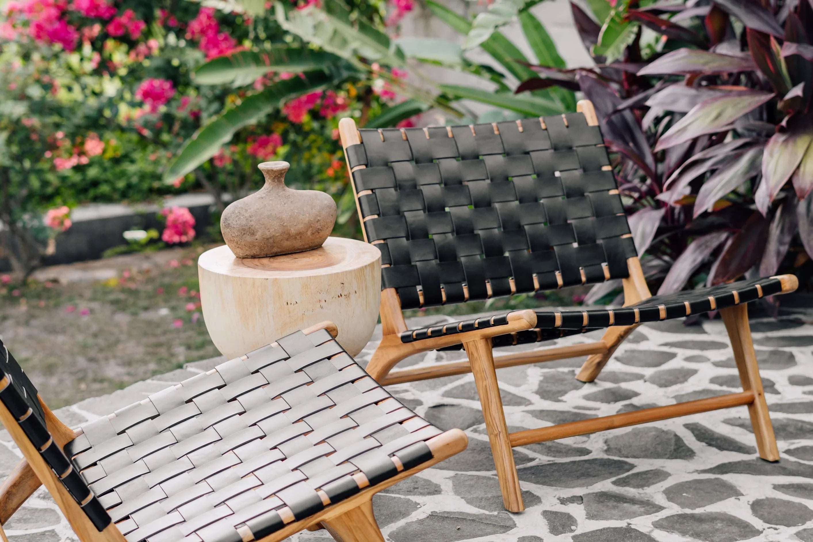 Handcrafted woven lounge chairs and side table with vase in a lush outdoor garden, Kayu Living