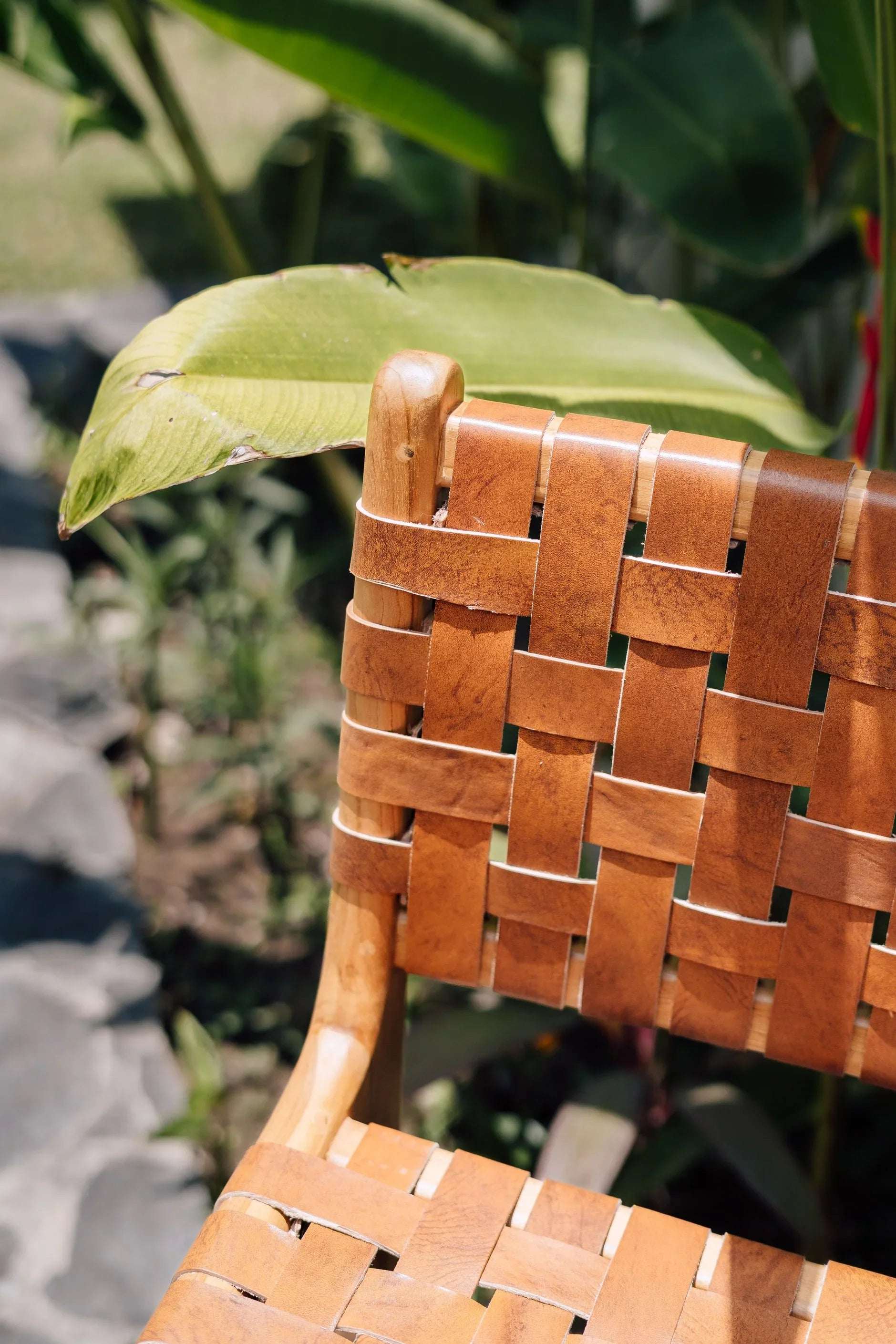 Handmade woven leather chair with wooden frame from Kayu Living, outdoors with green plants