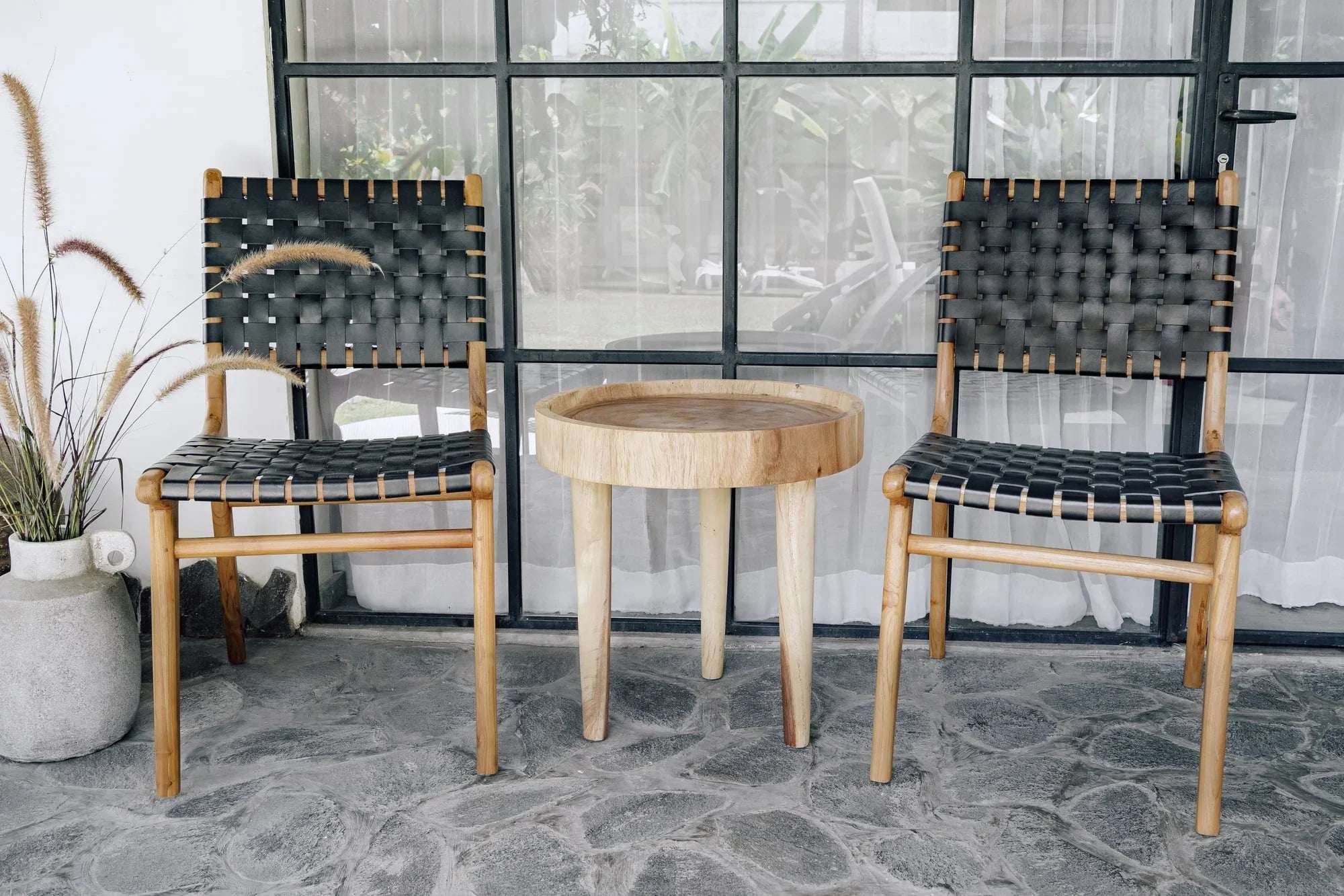 Handmade woven black chairs and round wooden table by Kayu Living on a stone patio