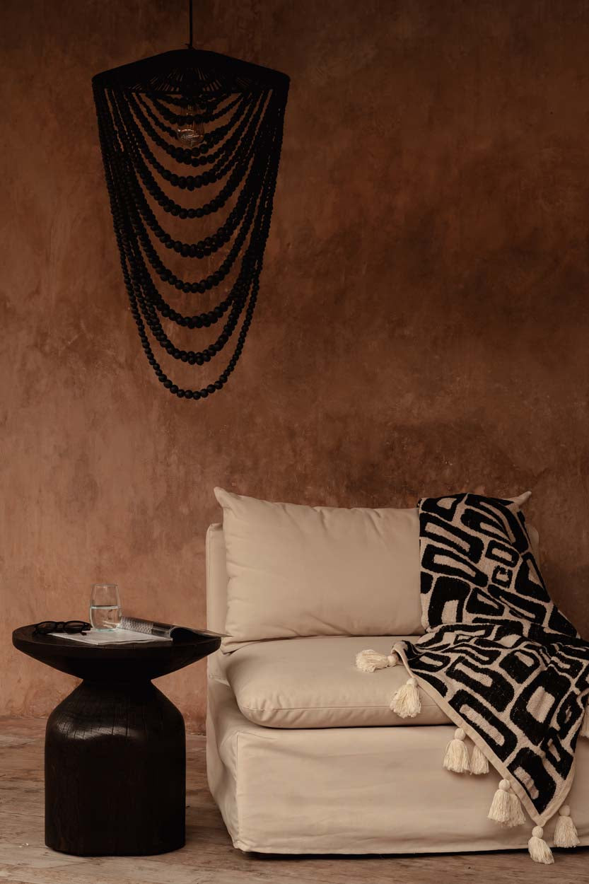 Kayu Living Aztec-pattern cotton throw in natural black with tassels draped over a beige sofa in a rustic room