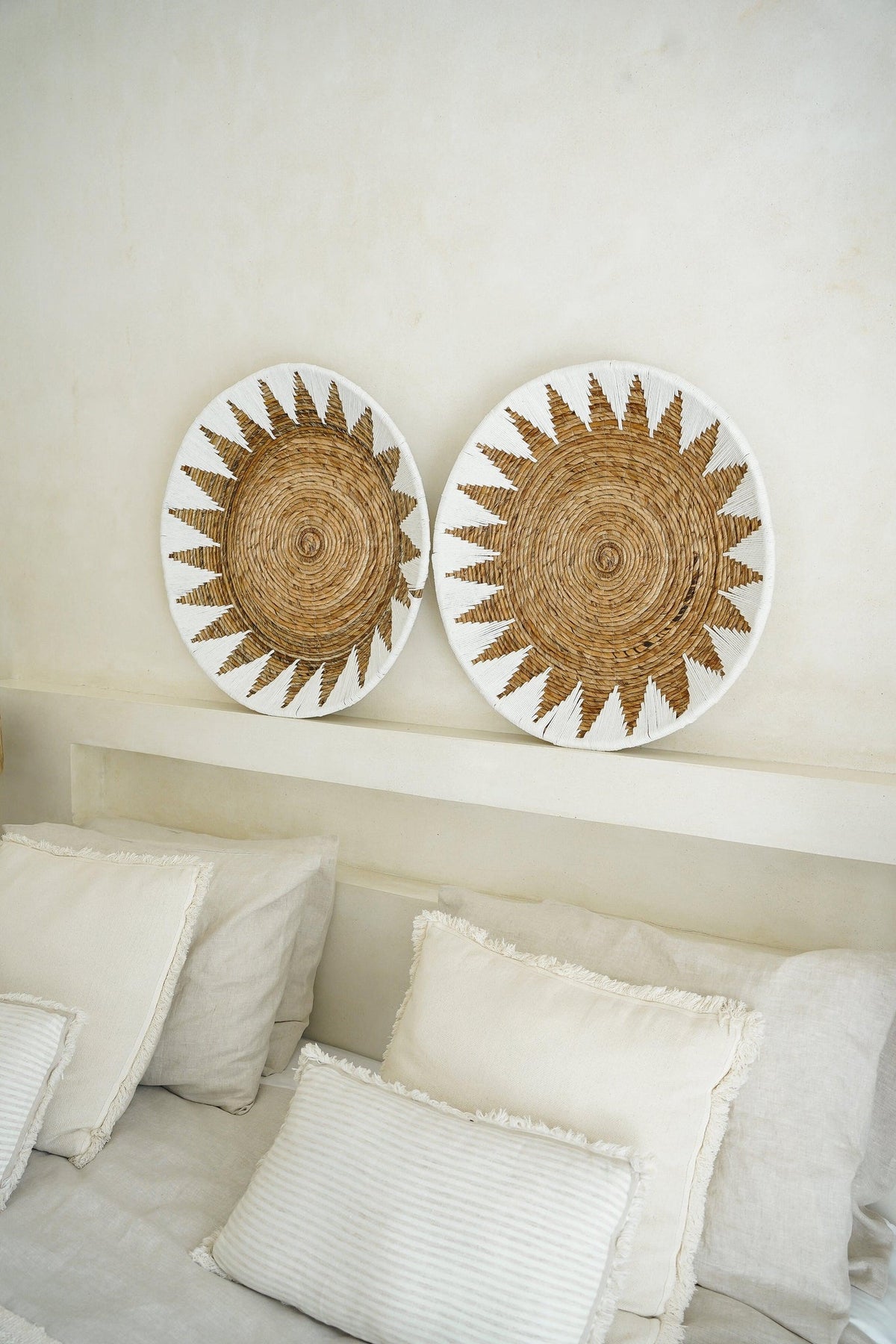 Two Kayu Living handcrafted bamboo star wall plates in white and brown displayed above a neutral bedroom headboard.