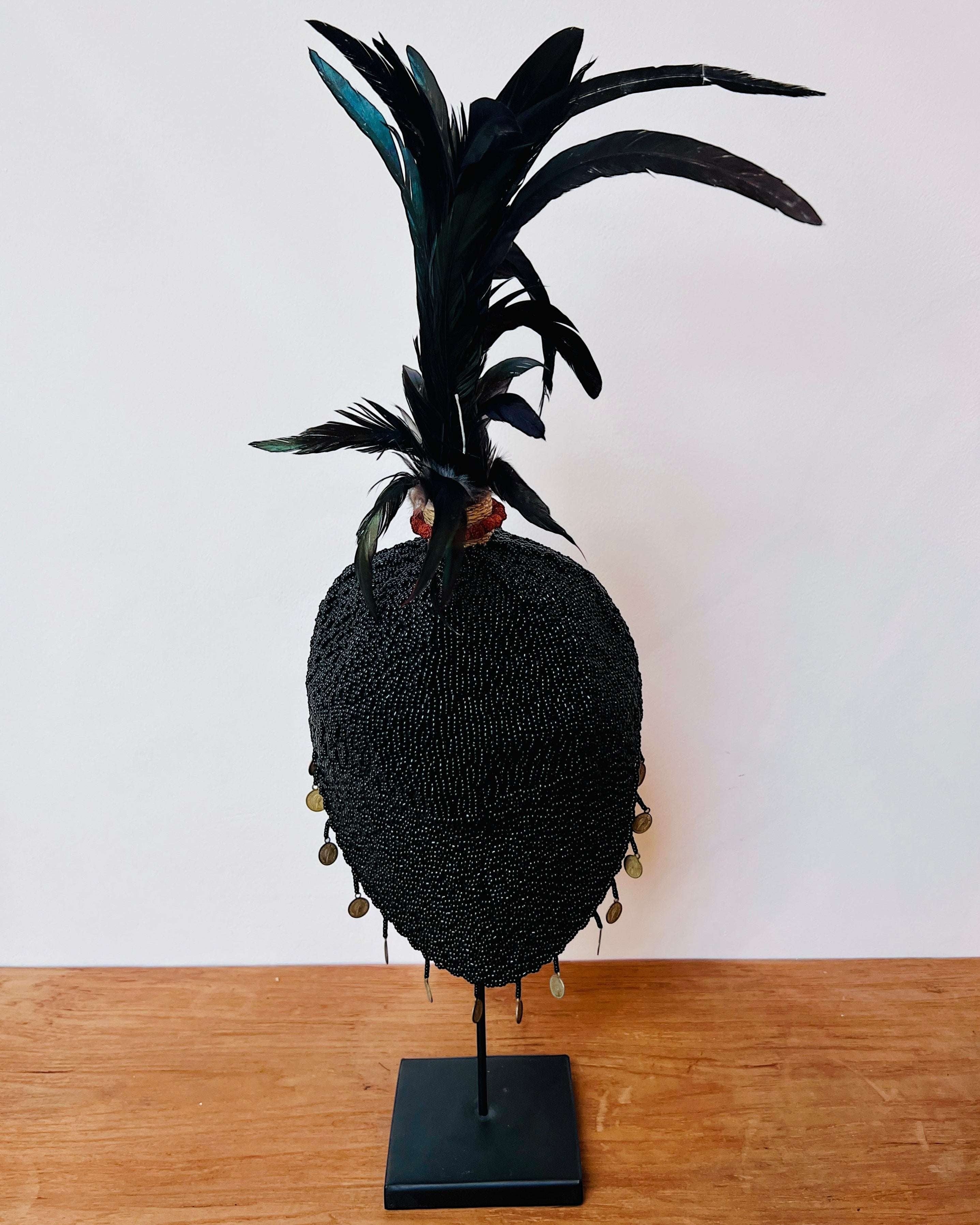 Kayu Living black beaded decorative hat with feathers and coins on a stand