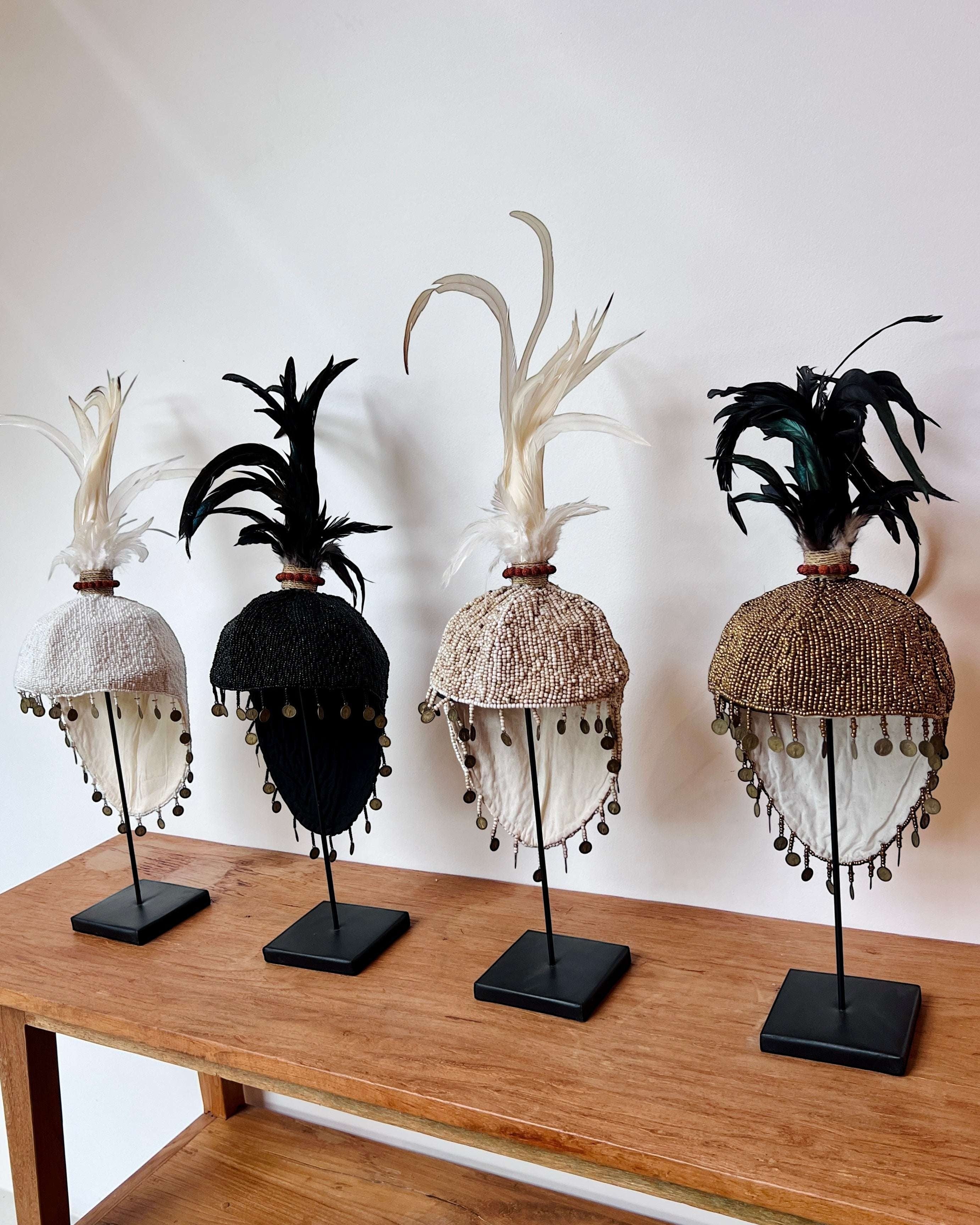 Kayu Living black beaded hat with feathers and coins on a stand, handmade decorative art.