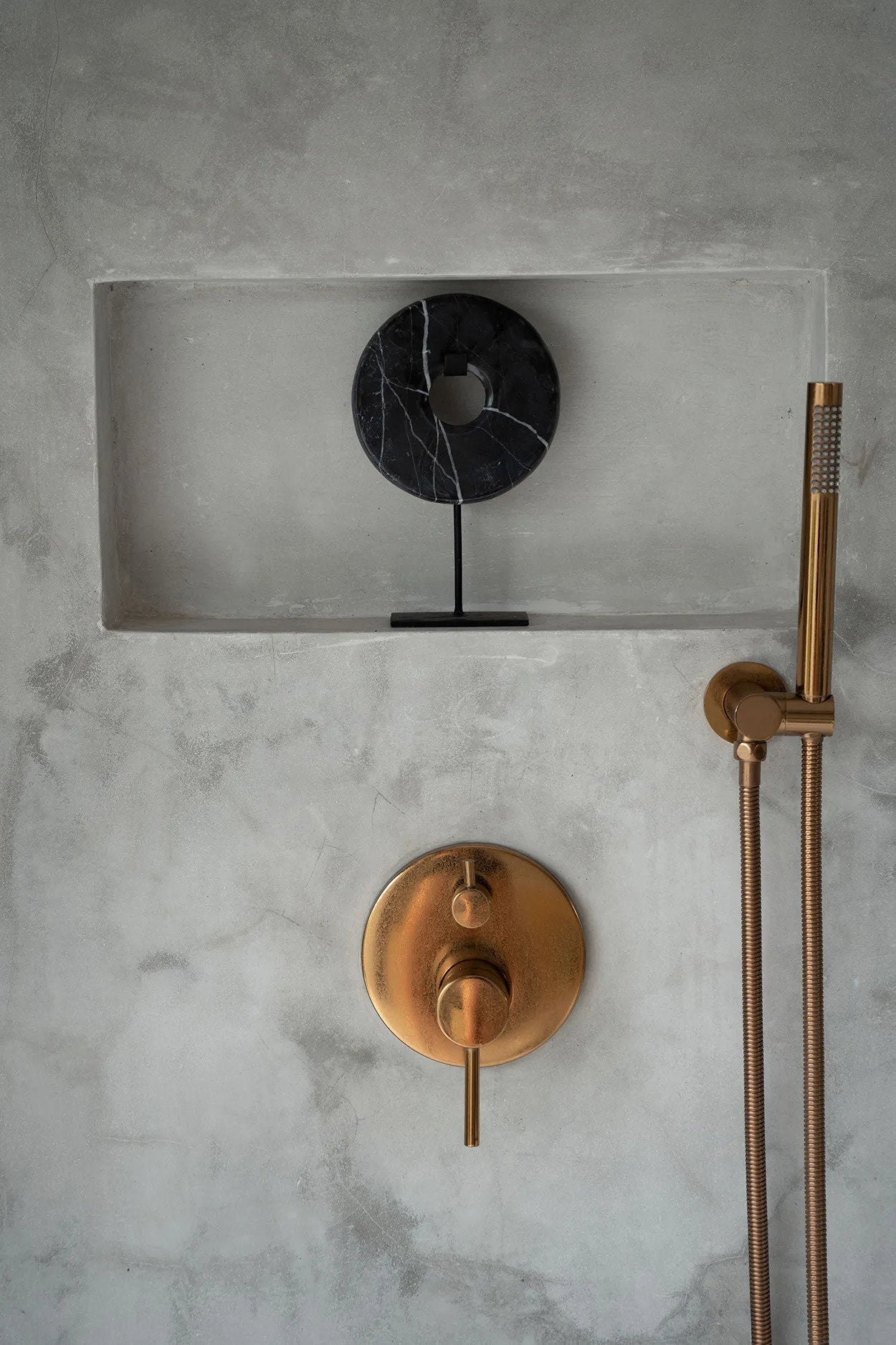Kayu Living small black marble disc sculpture on a sleek metal stand displayed in a modern concrete shower niche.