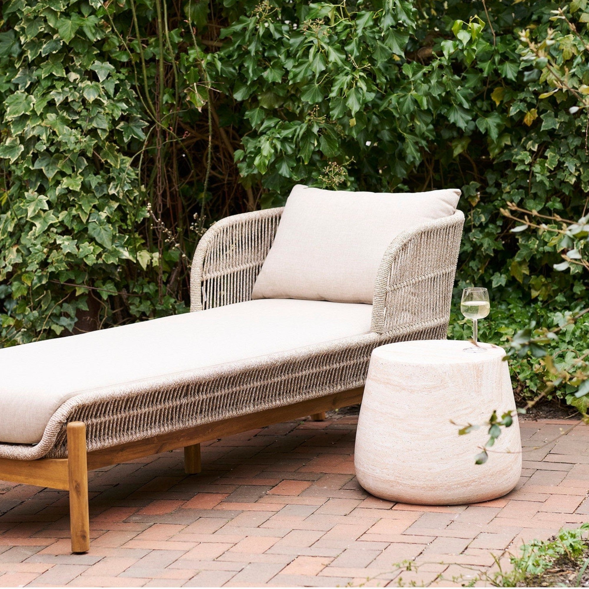 Kayu Living Bonn side table in natural fiberclay with a stone-like finish next to a wicker outdoor lounge chair.
