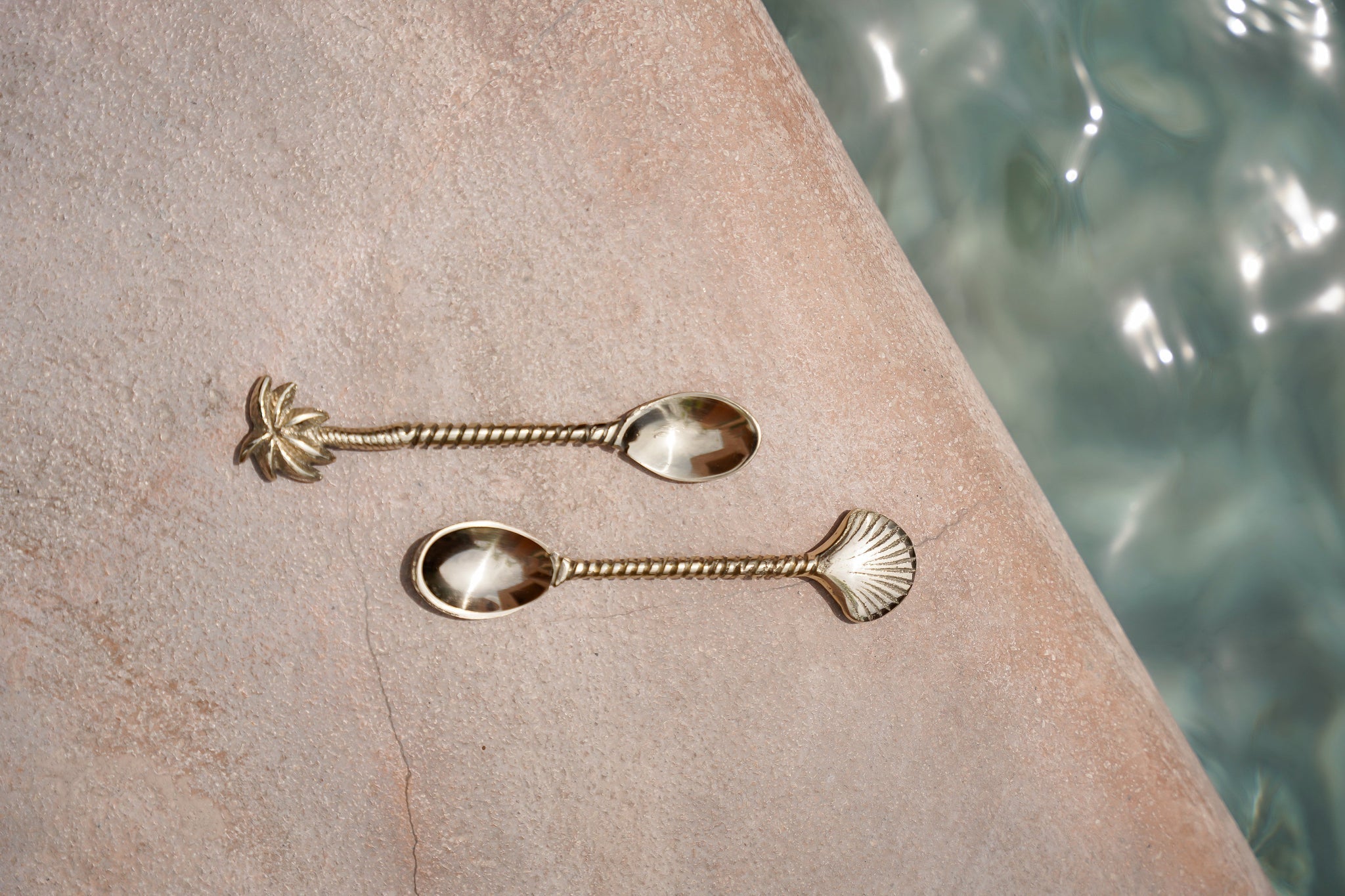 Kayu Living handcrafted brass spoons with palm tree and seashell motifs on a textured stone surface