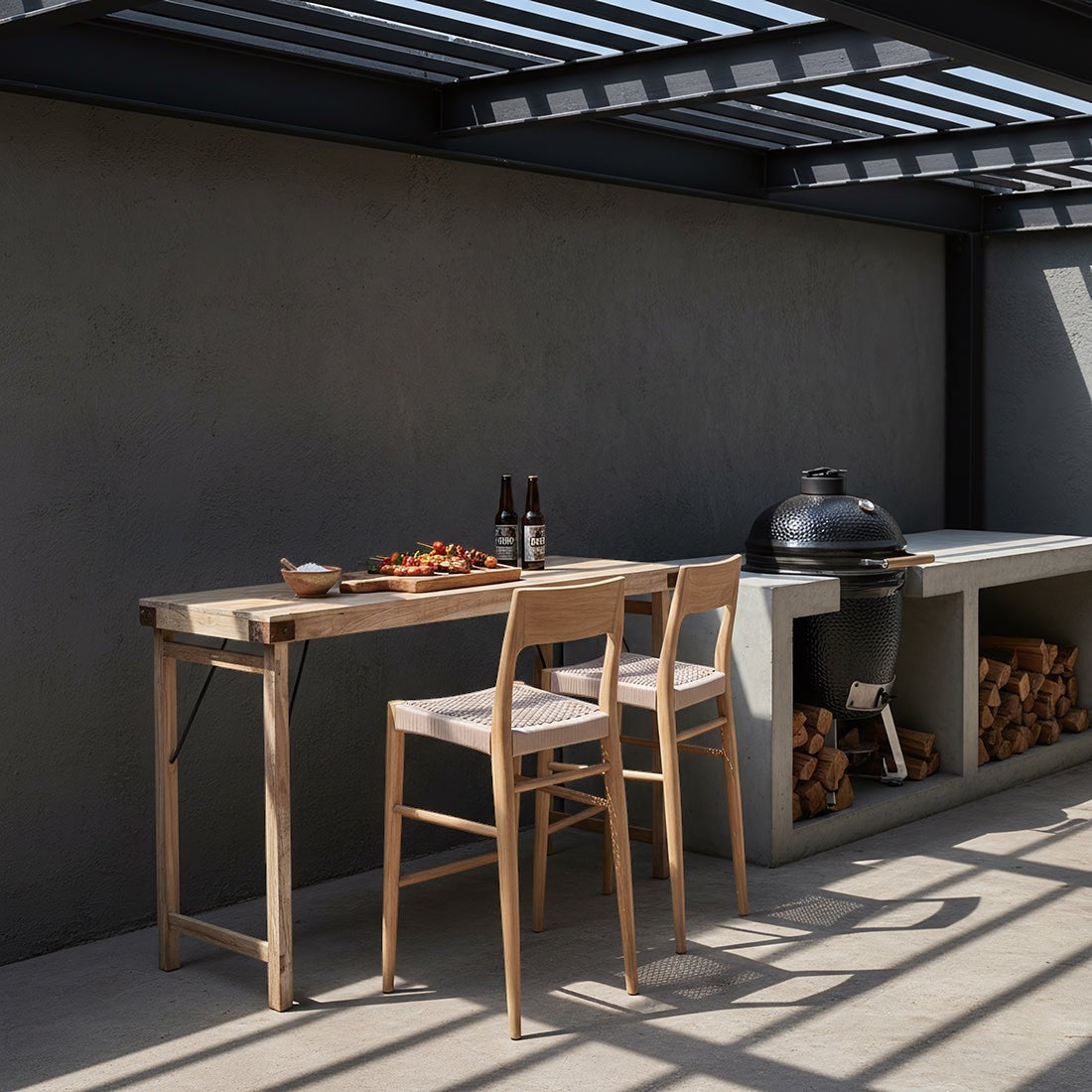 Kayu Living Freya teak bar stools with beige woven rope seats placed at a wooden table on a modern outdoor patio.