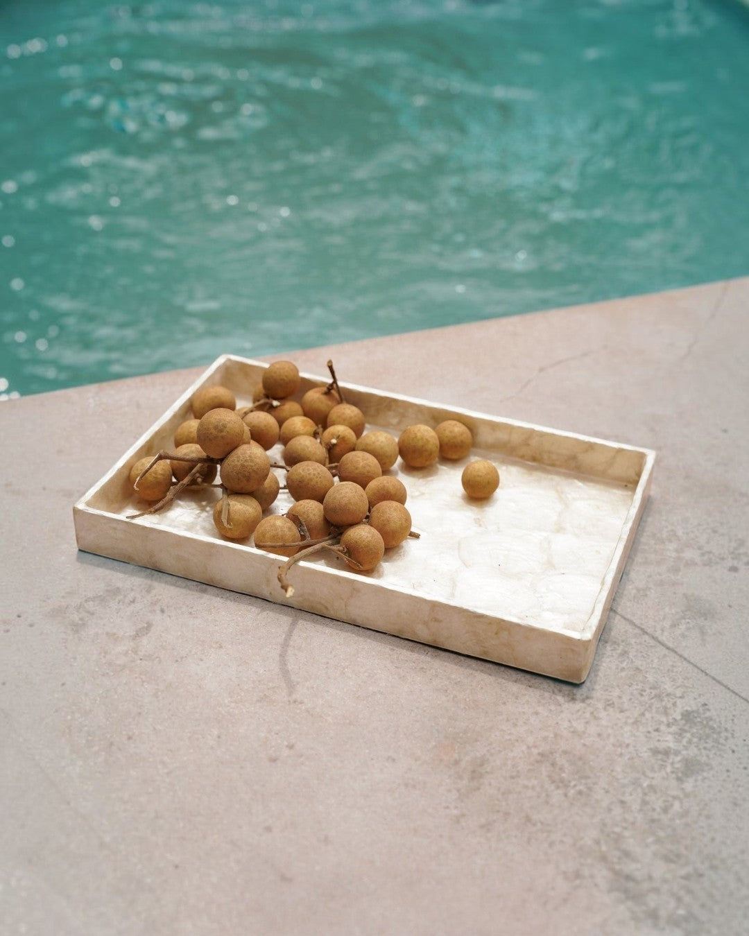 Kayu Living handmade rectangular gold Capiz shell tray holding longan fruit beside a pool
