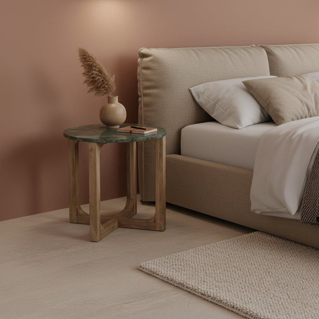 Kayu Living round green marble side table with a mango wood base next to a beige upholstered bed in a bedroom.