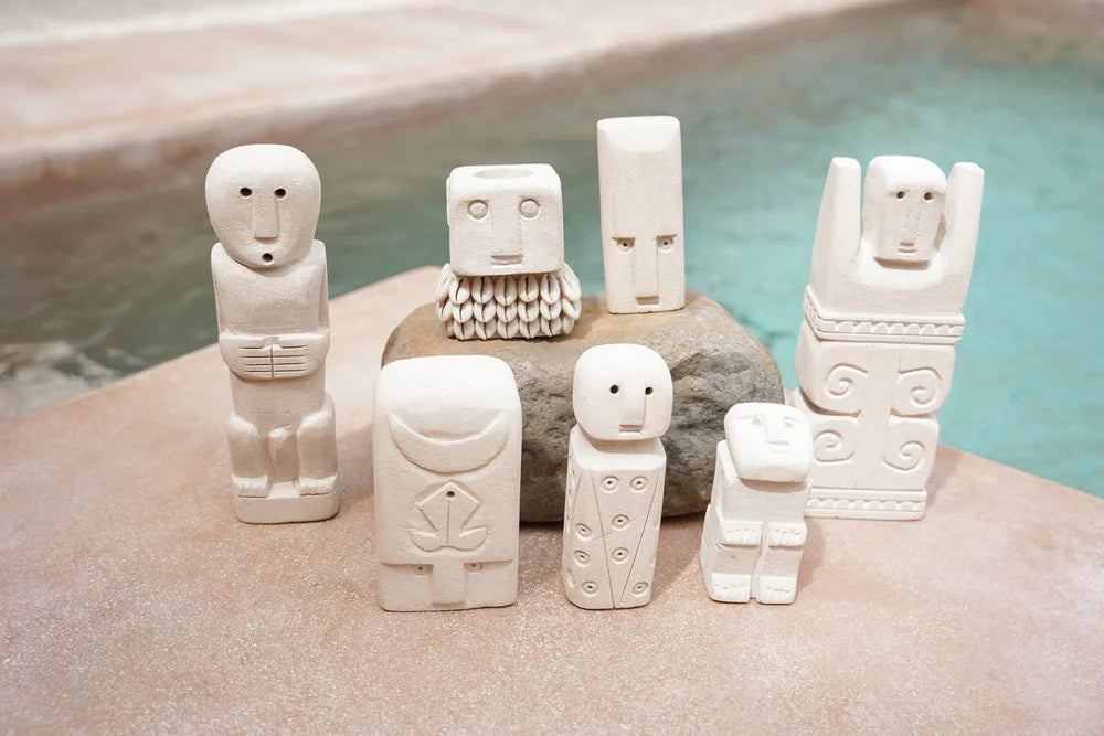 Kayu Living handcrafted Balinese stone guardian figurines with unique carved faces and symbols on a stone surface.