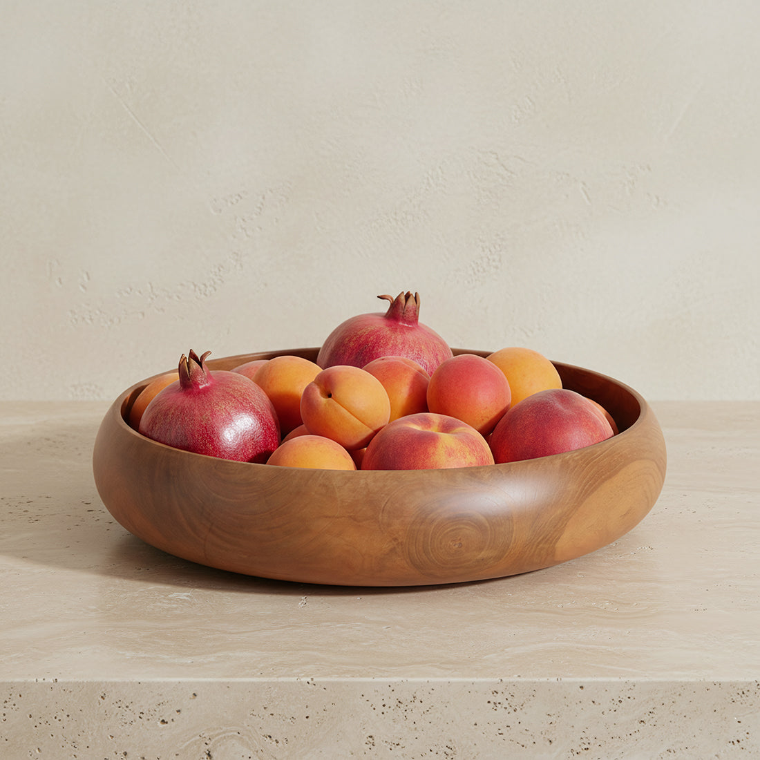 Kayu Living large 37cm solid teak wood bowl filled with fresh pomegranates and apricots on a stone surface