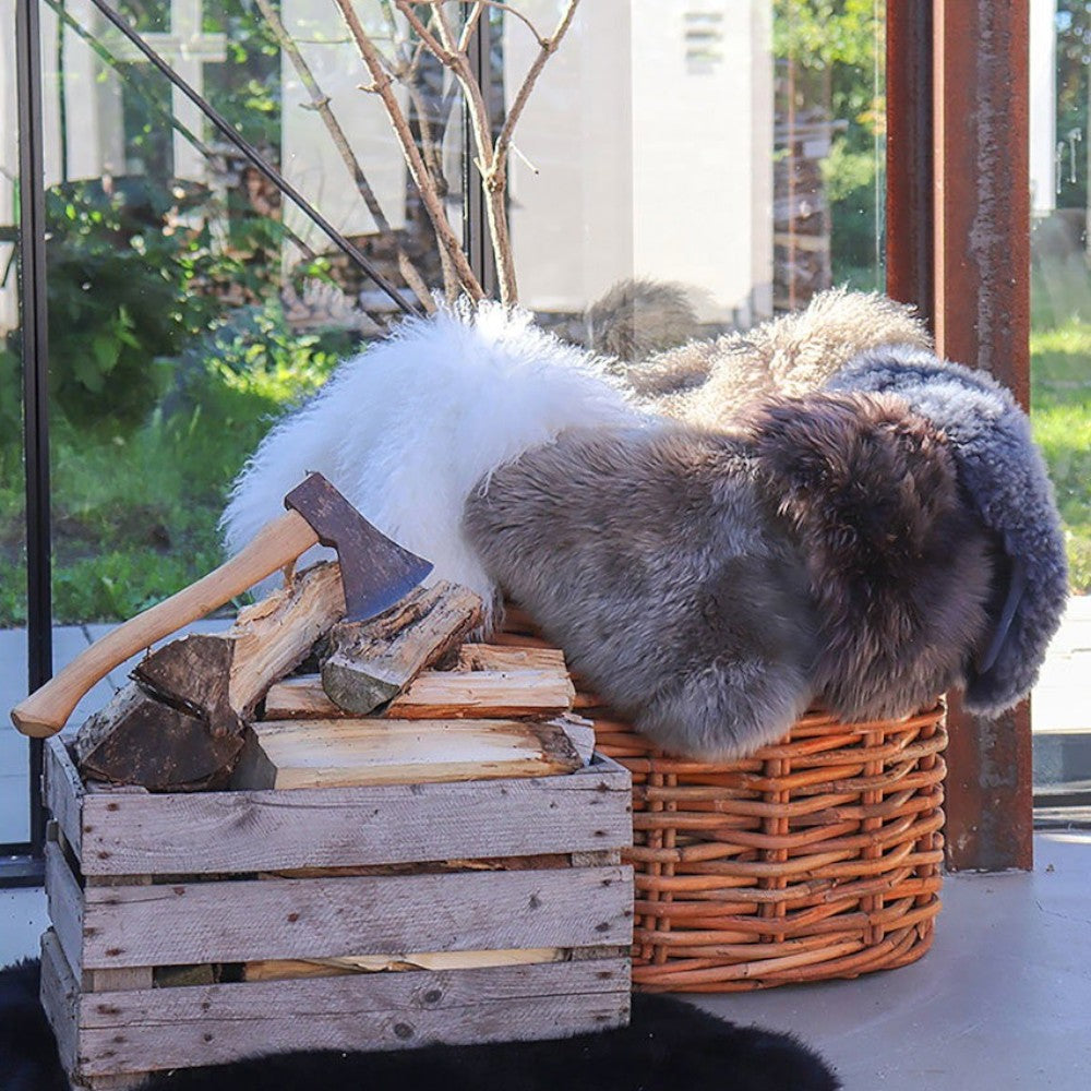 Kayu Living mushroom coloured genuine lambskin rug draped over a wicker basket next to firewood and an axe