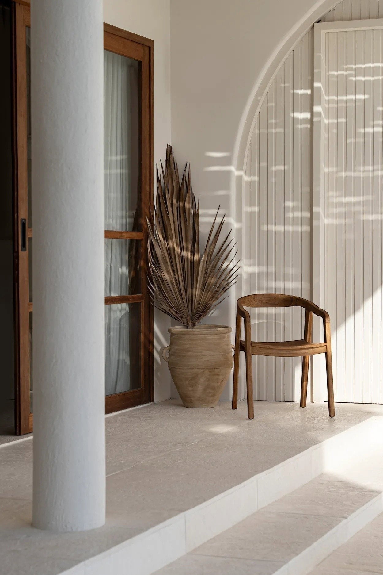 Kayu Living Nihi Oka outdoor dining chair made of natural teak wood with a curved back and armrests.