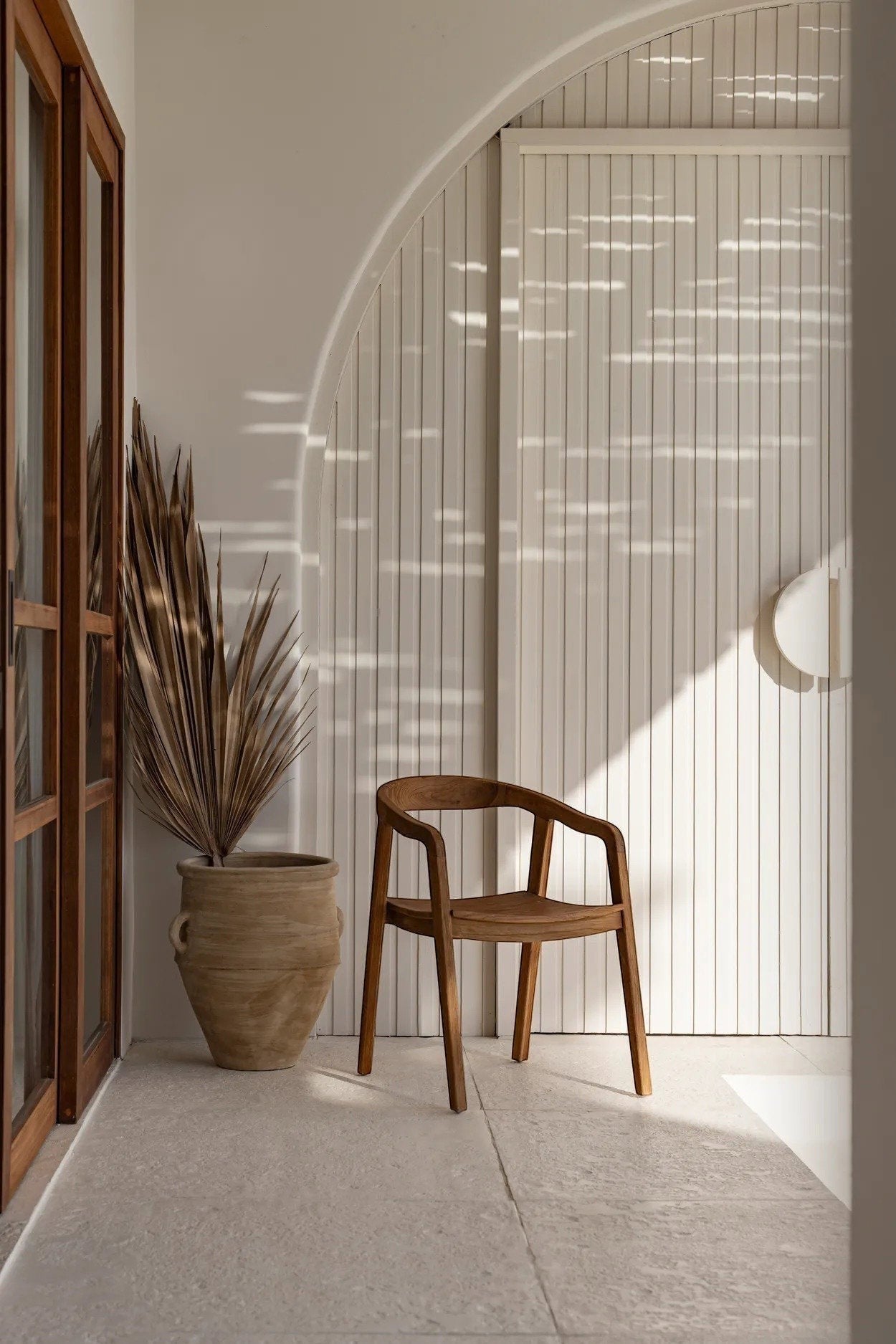 Kayu Living Nihi Oka outdoor dining chair made of natural teak wood with a curved back and armrests.