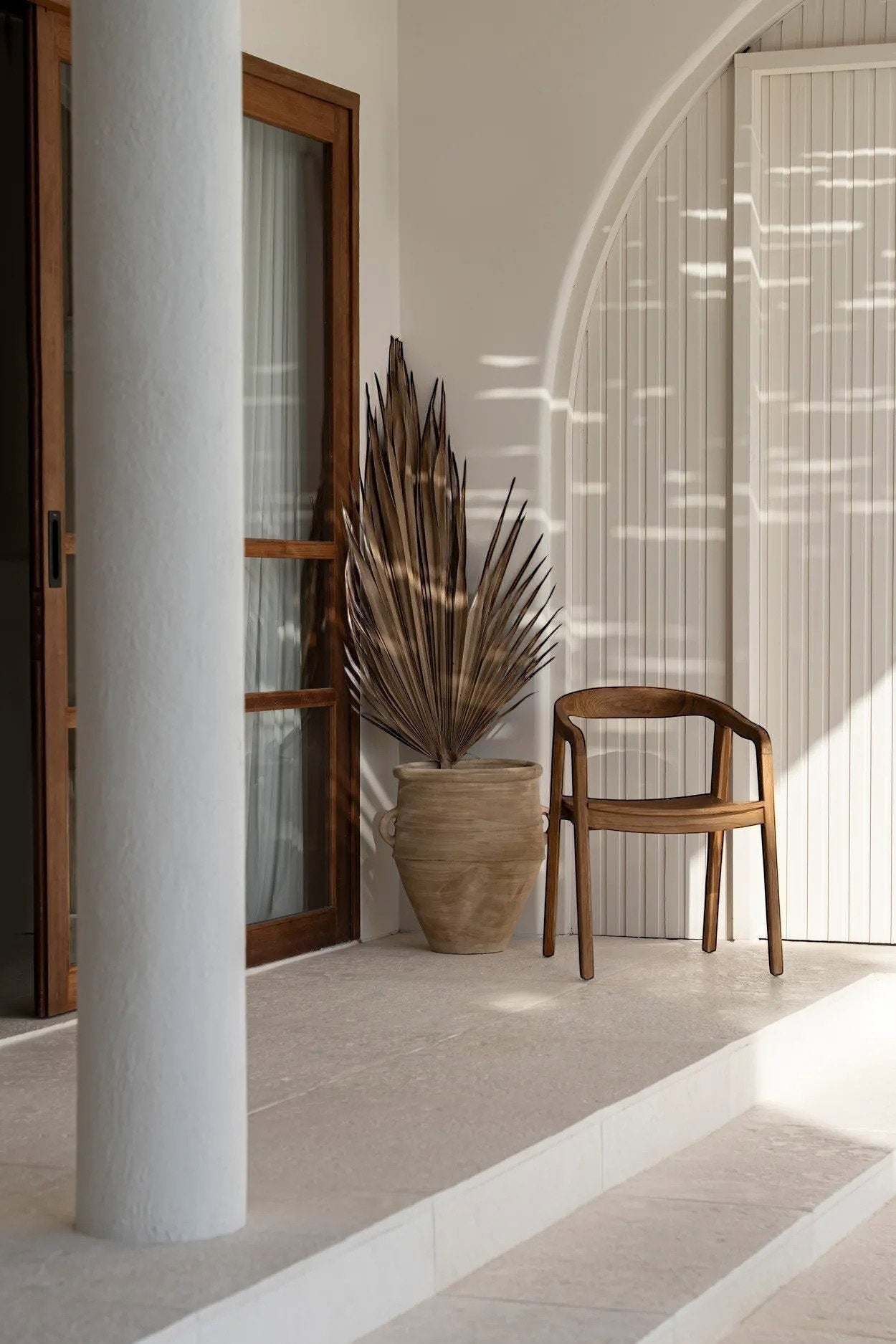 Kayu Living Nihi Oka outdoor dining chair made of natural teak wood with a curved back and armrests.