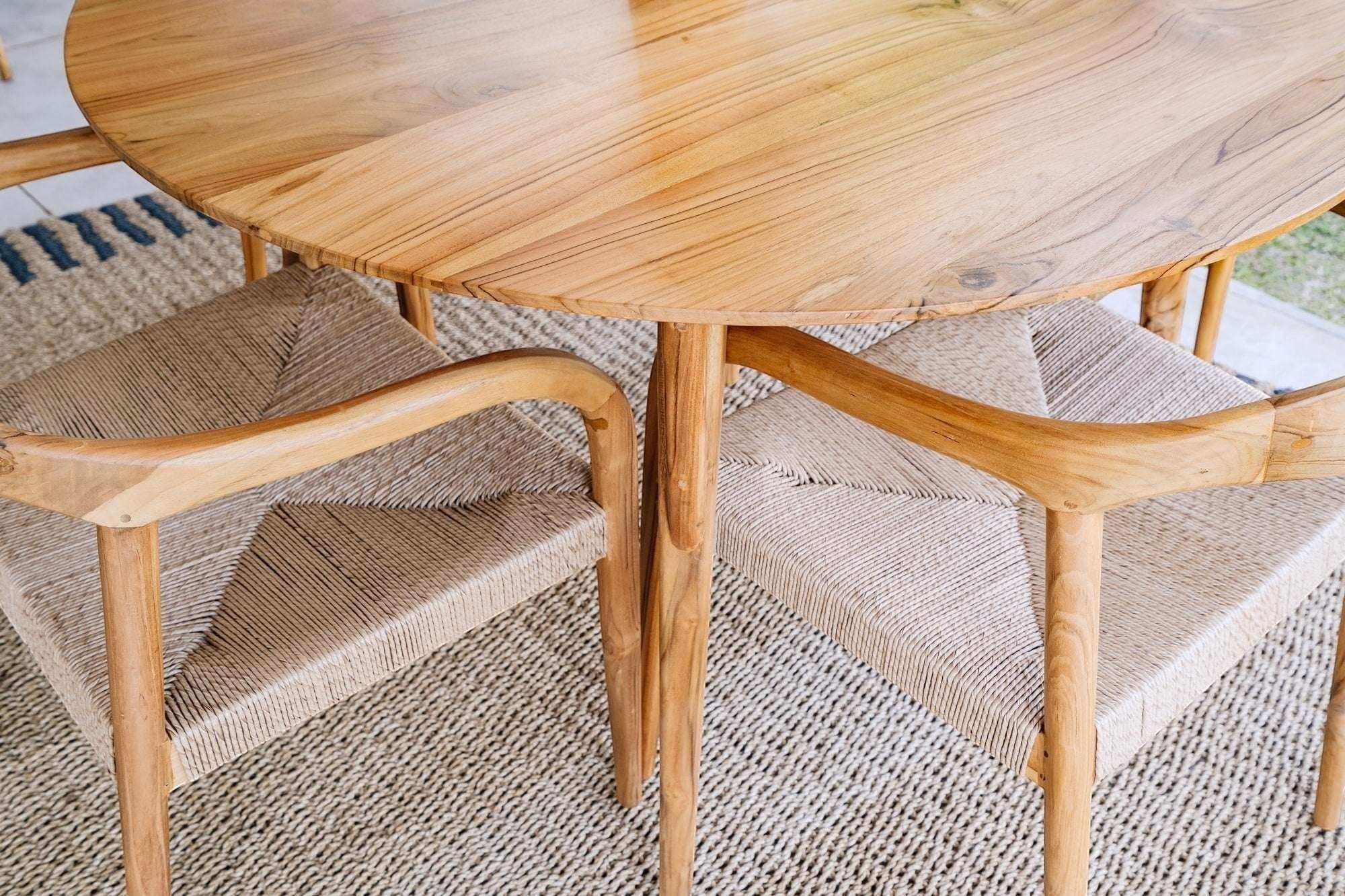 Kayu Living Pantai round teak dining table, 120 cm, with natural wood grain and woven chairs.