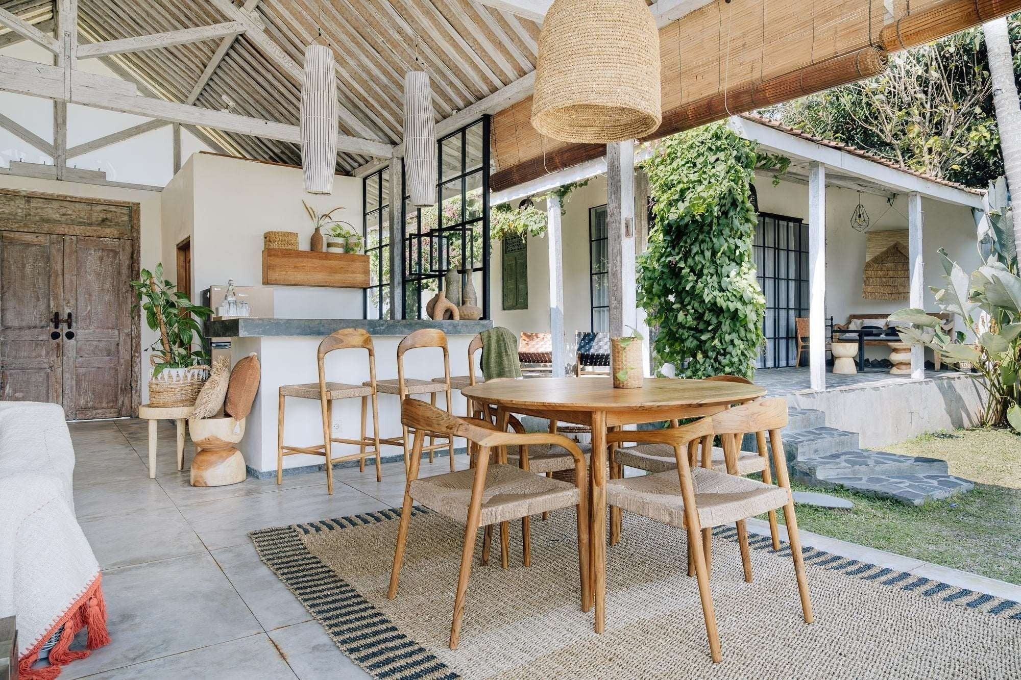 Kayu Living Pantai round teak dining table, 120 cm, with natural wood grain and four woven chairs.