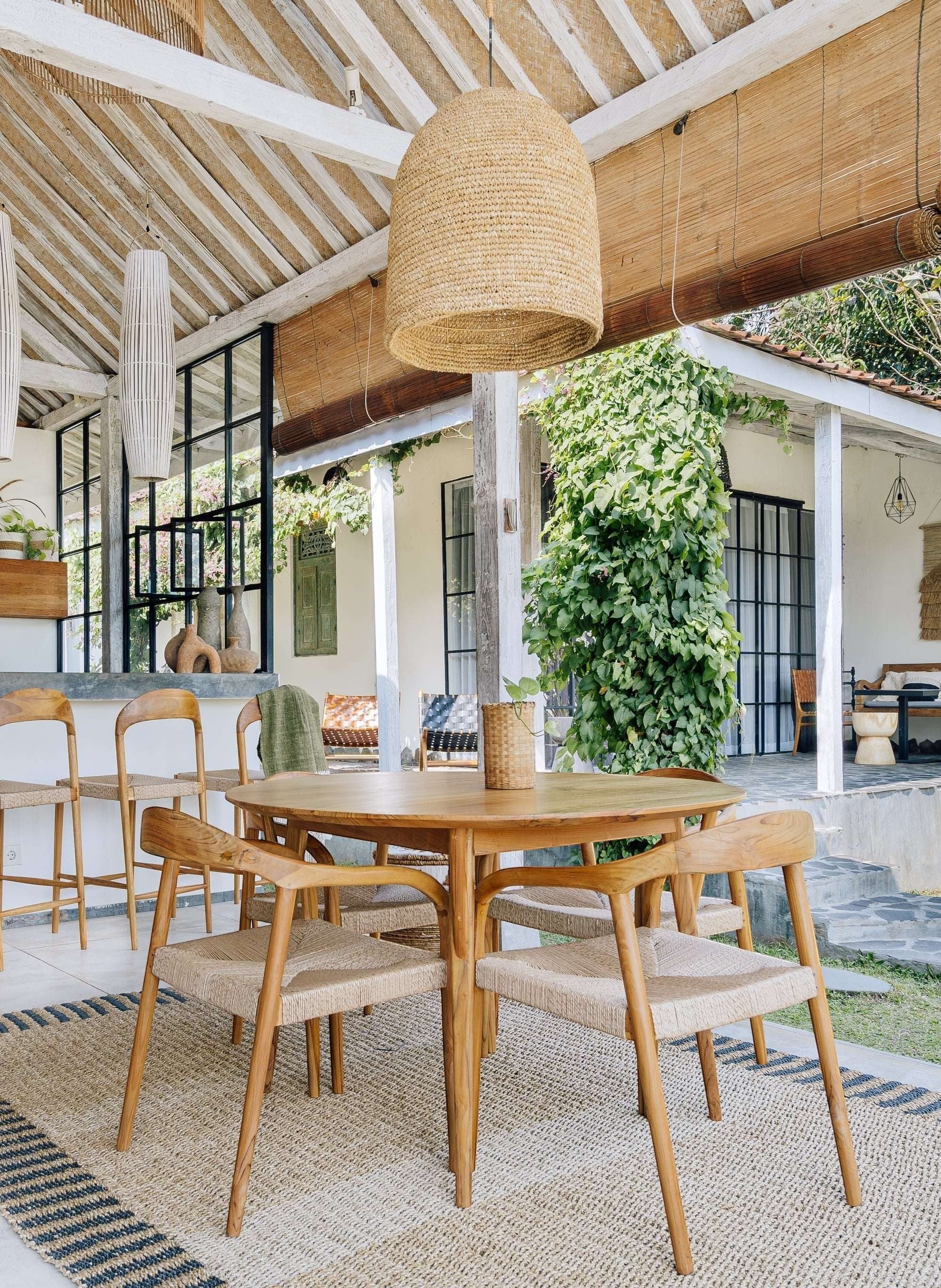 Kayu Living Pantai round 120 cm teak dining table with woven chairs, natural wood grain and earthy tones.