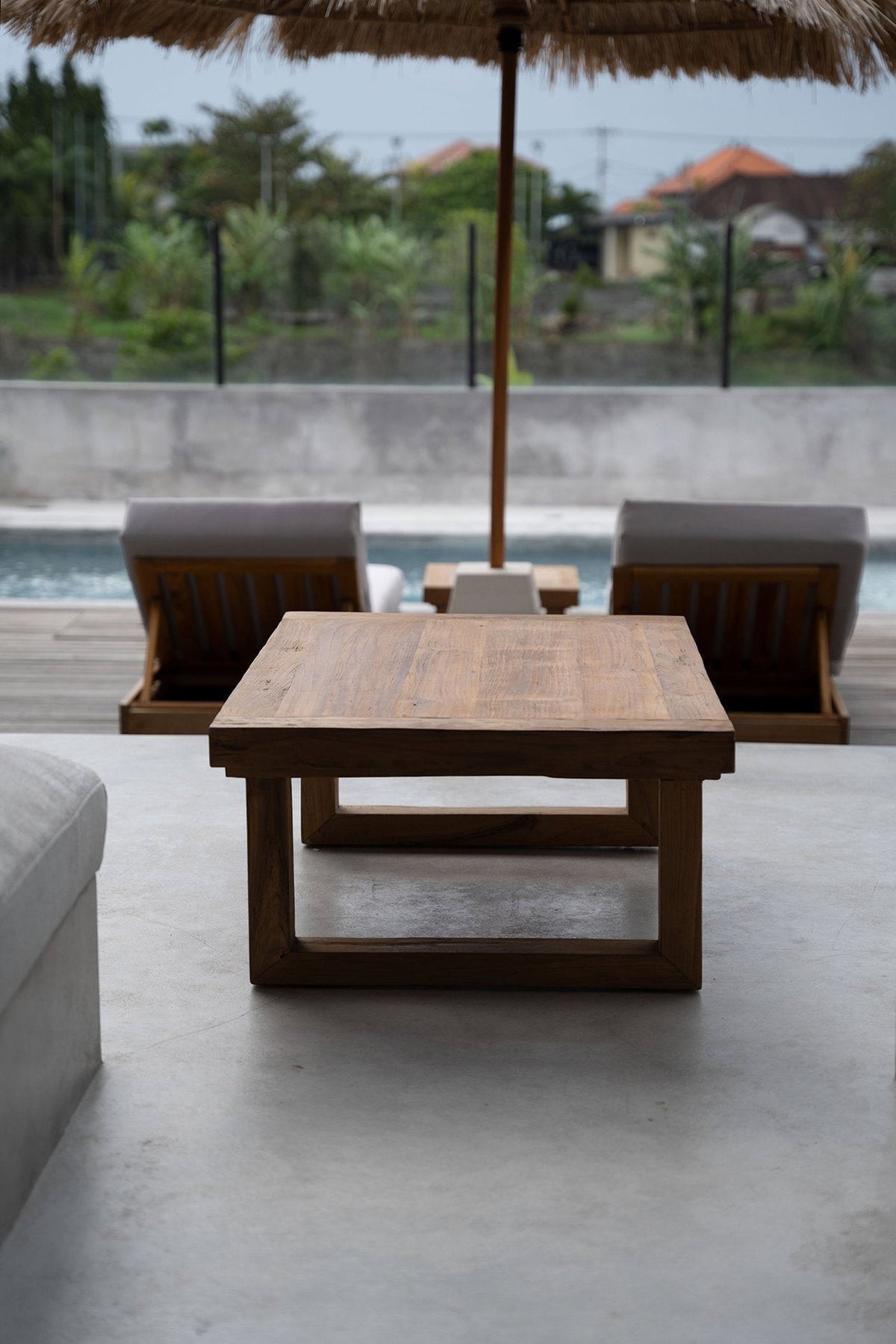 Kayu Living reclaimed teak coffee table with a natural wood finish, set on a patio overlooking a swimming pool.