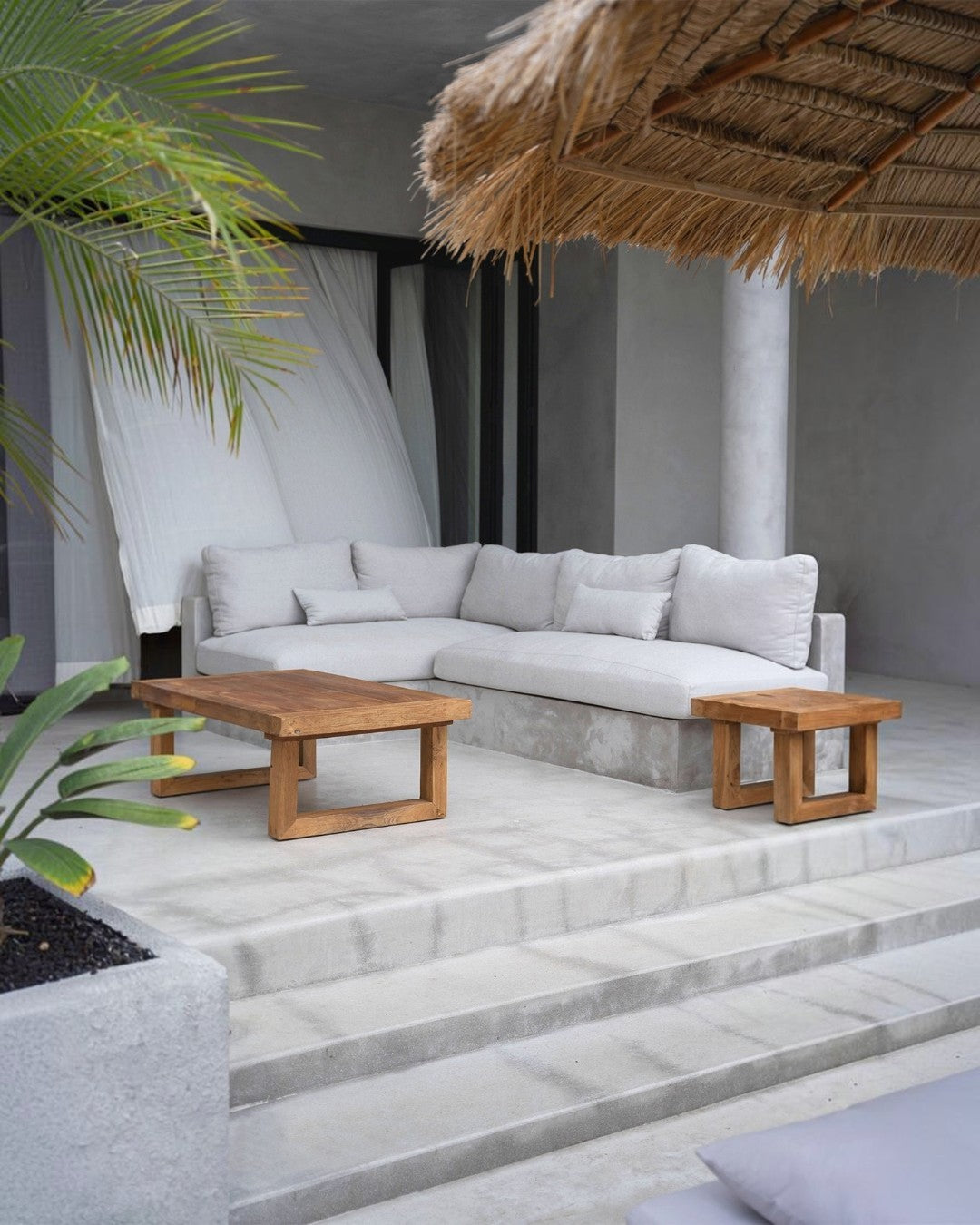 Kayu Living reclaimed teak coffee table and matching side table on a modern outdoor patio with a thatched roof.