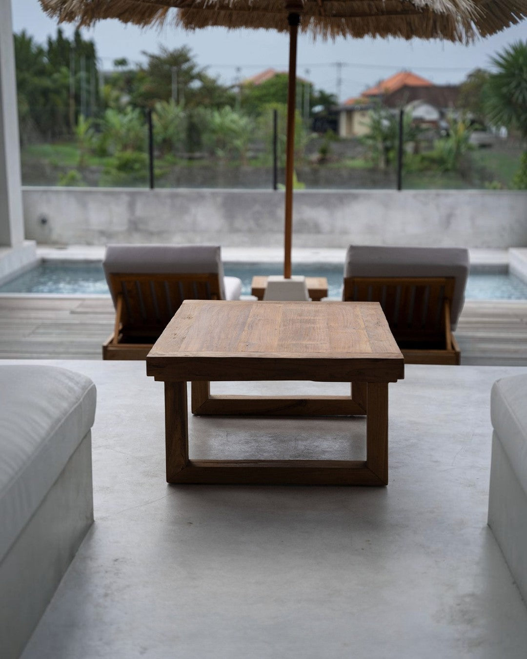 Kayu Living reclaimed teak coffee table with a natural finish, positioned on a patio overlooking a swimming pool.