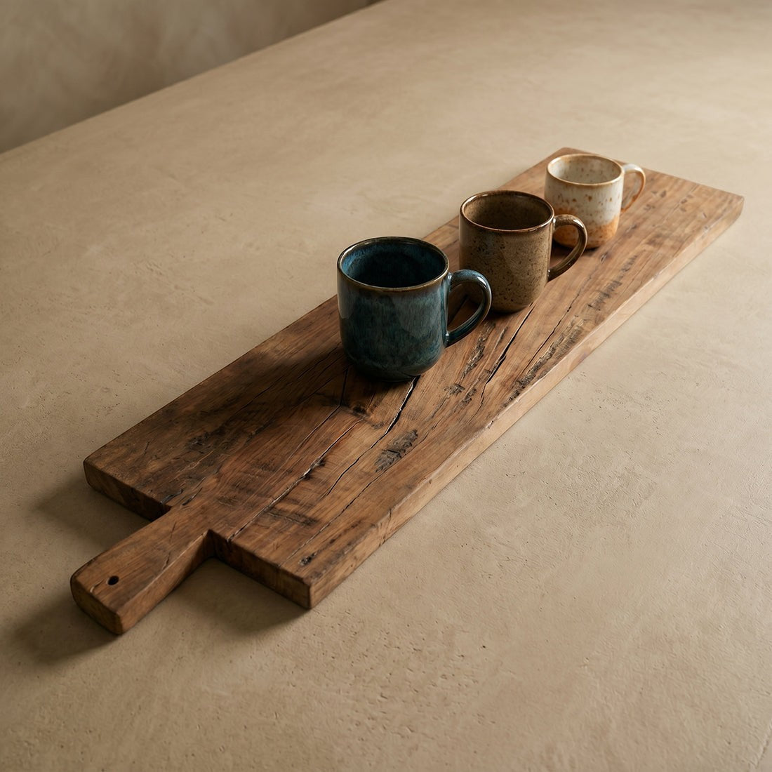Kayu Living 90 cm handcrafted reclaimed wood snack board with three rustic ceramic mugs on a beige surface.