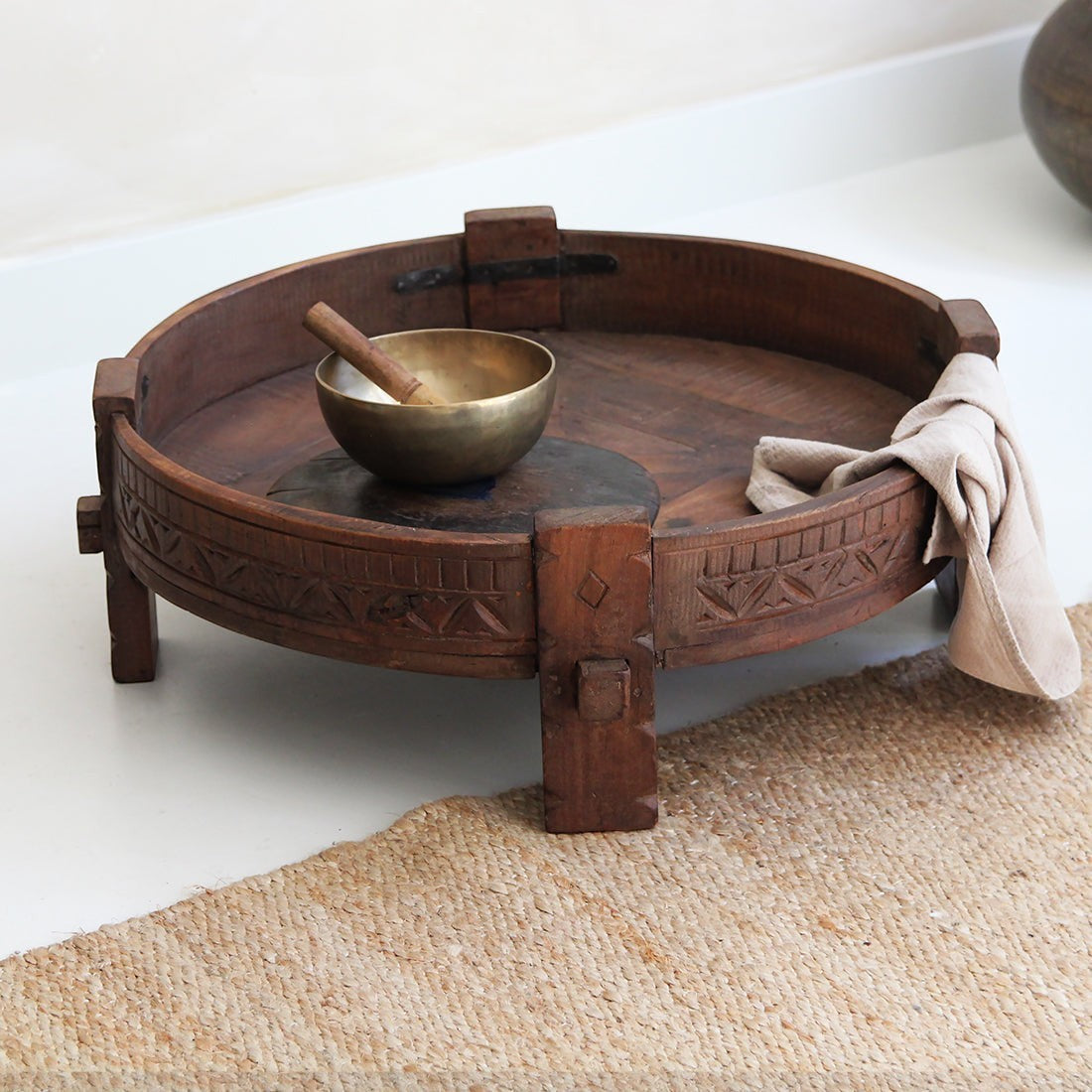 Kayu Living round recycled hardwood Chakki side table with carved details and a rich patina on a jute rug.