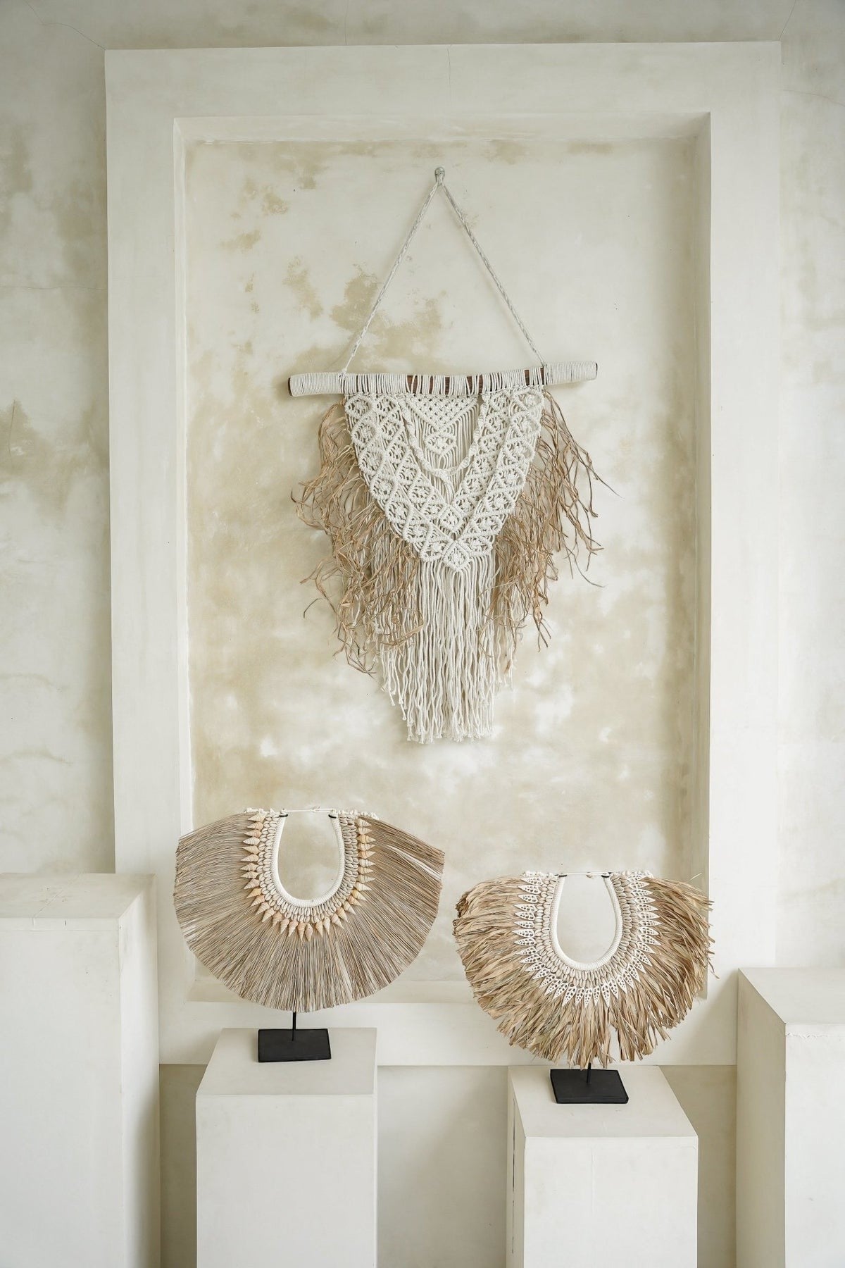 Kayu Living handcrafted seagrass and shell decor on black stands with a matching macrame wall hanging in a neutral room
