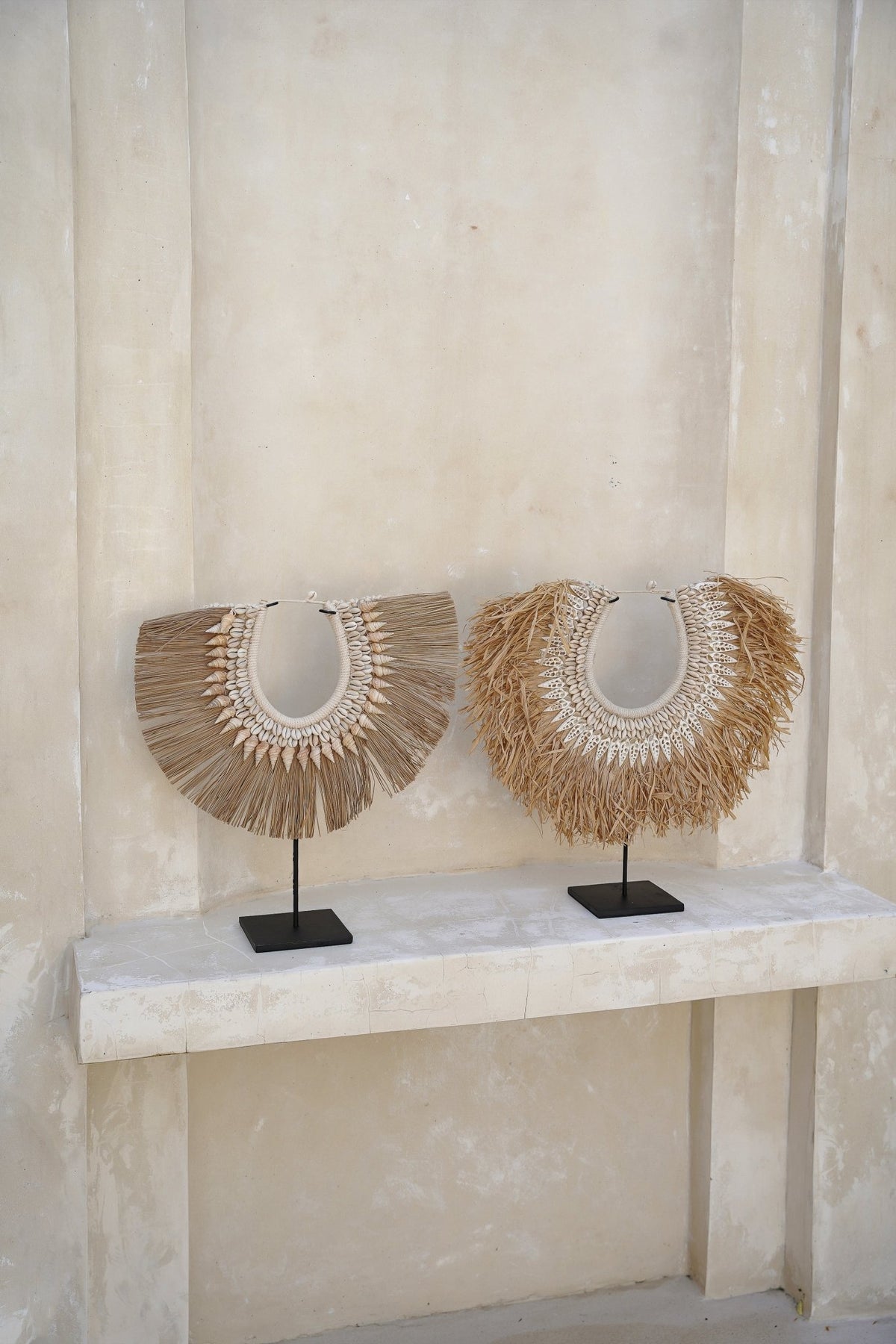 Kayu Living handmade seagrass and shell hangers on black stands, featuring natural textures and neutral tones.