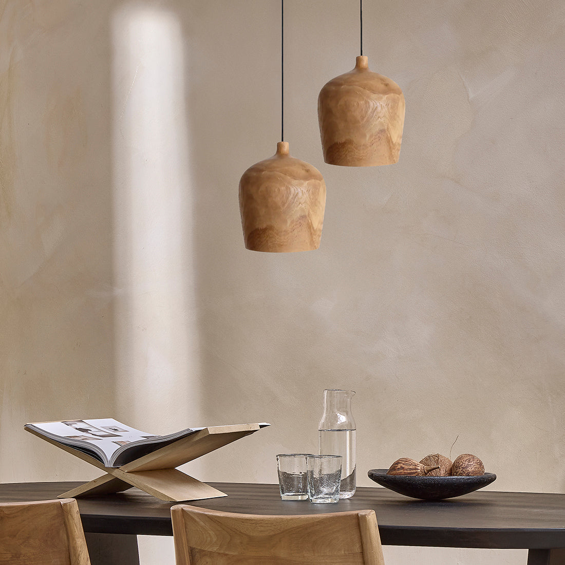 Kayu Living Sirocco Bottle pendant lamps in solid teak wood hanging above a dining table with natural wood grain.