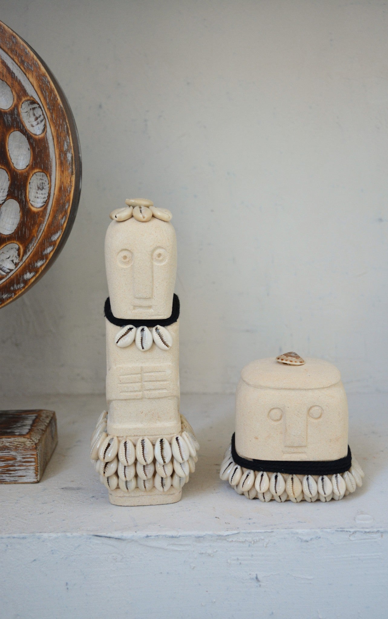 Kayu Living handmade natural stone figurines decorated with cowrie shells and black fabric accents on a white shelf.