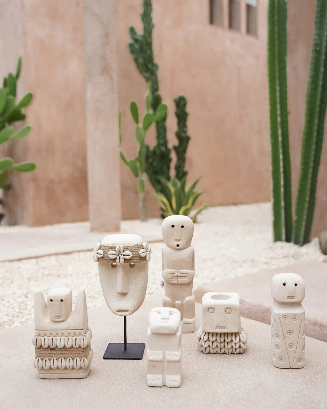 Kayu Living handcrafted stone figurines with shell accents and a white mask on a stand in a desert-inspired setting.