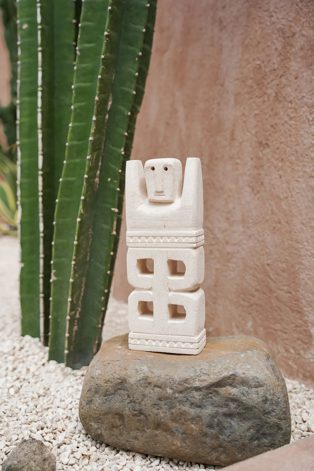 Kayu Living hand-carved stone guardian figurine with geometric carvings, displayed on a rock near a tall cactus.