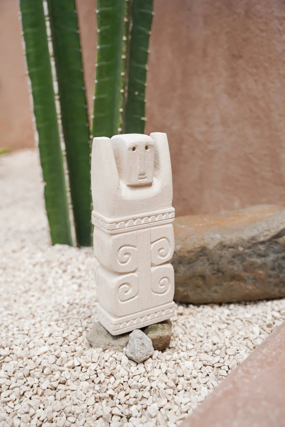 Kayu Living handcrafted Balinese stone guardian figurine with carved spiral details standing on gravel.