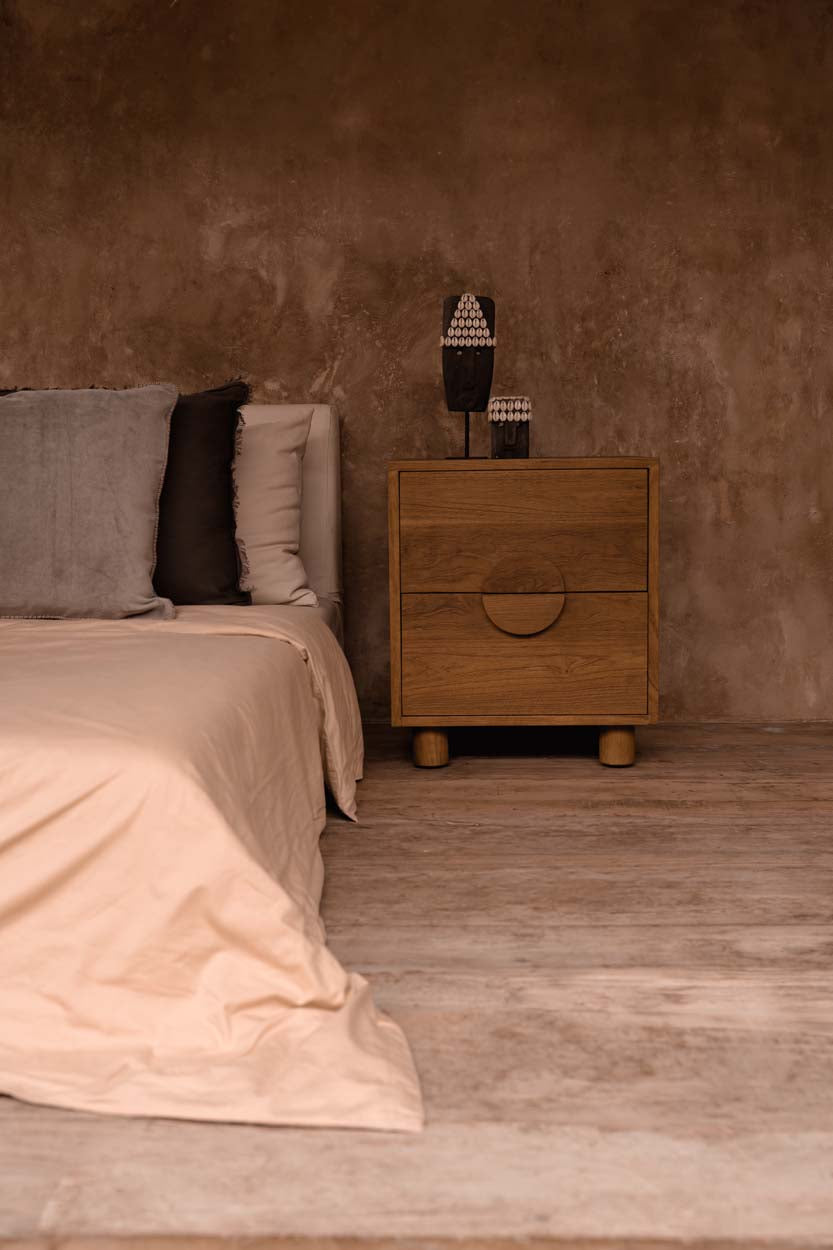 Kayu Living hand-carved grey sandstone Sumba stone statue on a wooden stand displayed on a bedside table.