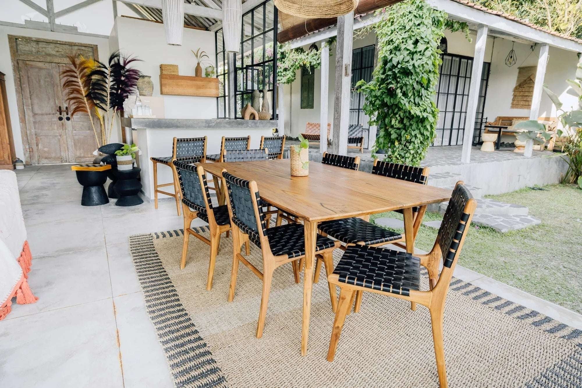 Kayu Living Berawa teak dining table 180x100 cm with natural grain and warm tones, paired with black woven chairs.