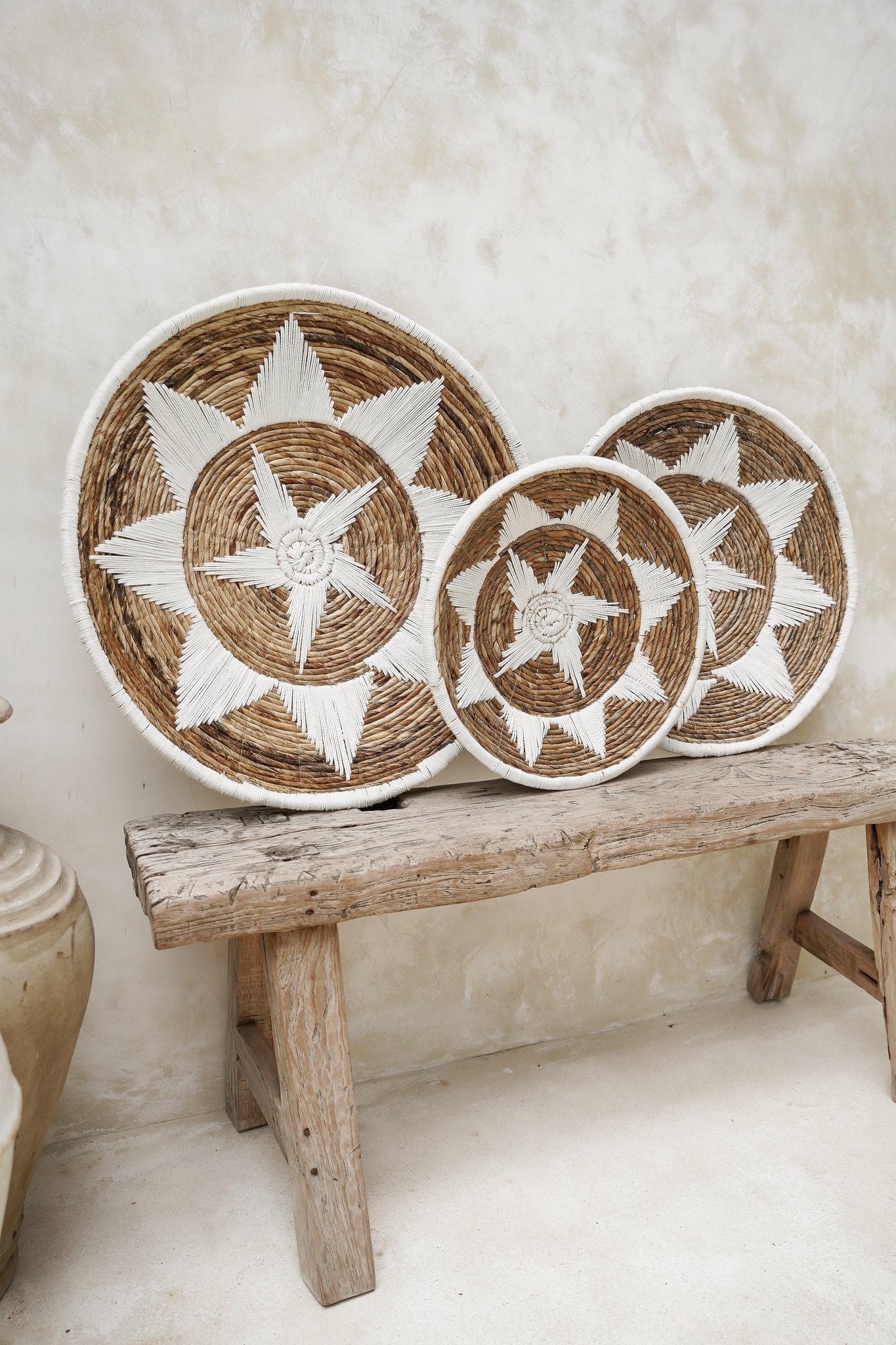 Kayu Living Uluwatu handmade brown and white banana leaf and cotton wall baskets displayed on a rustic wooden bench.