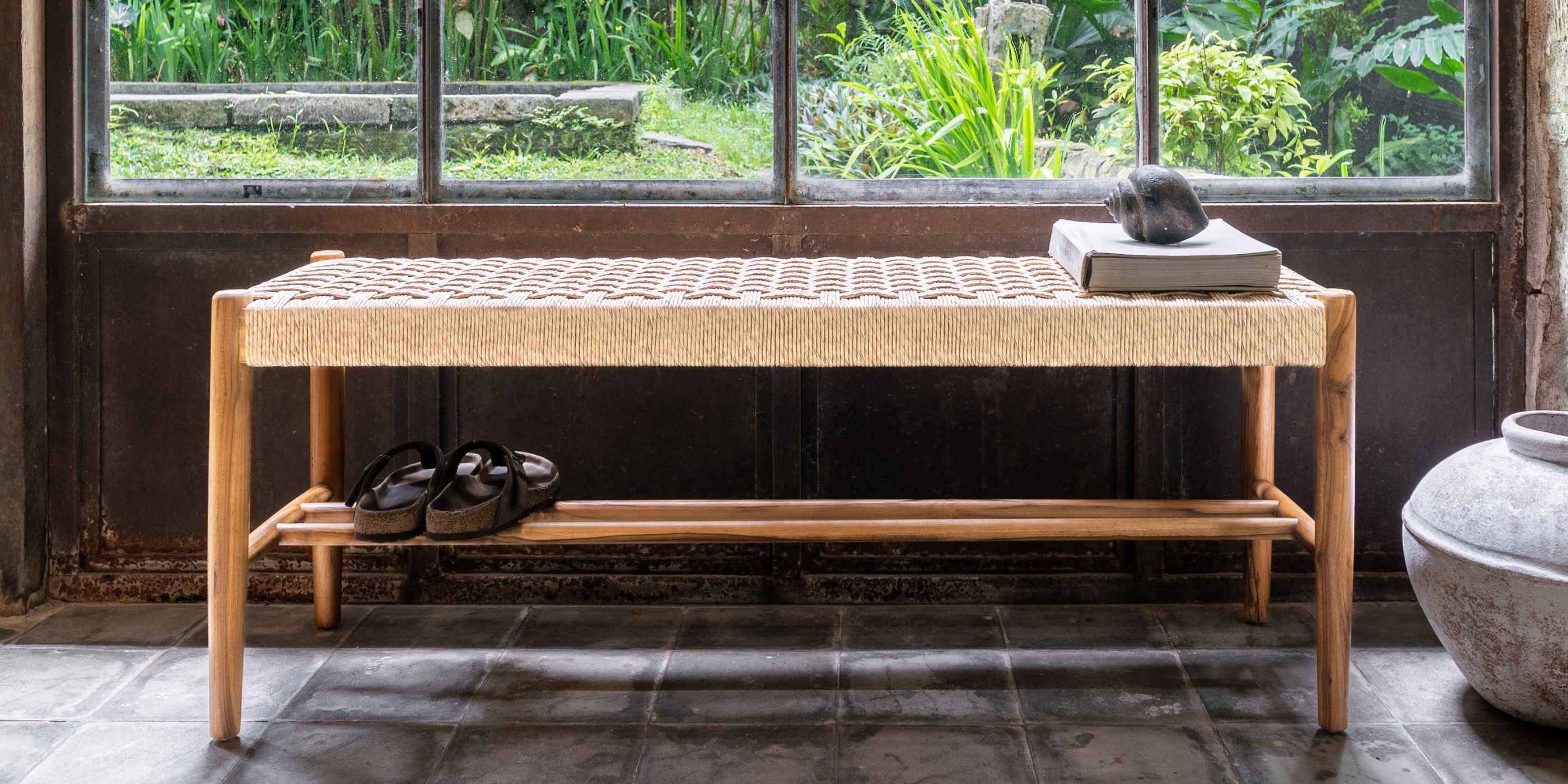 Wooden bench with woven top and shoe rack against a window with greenery view
