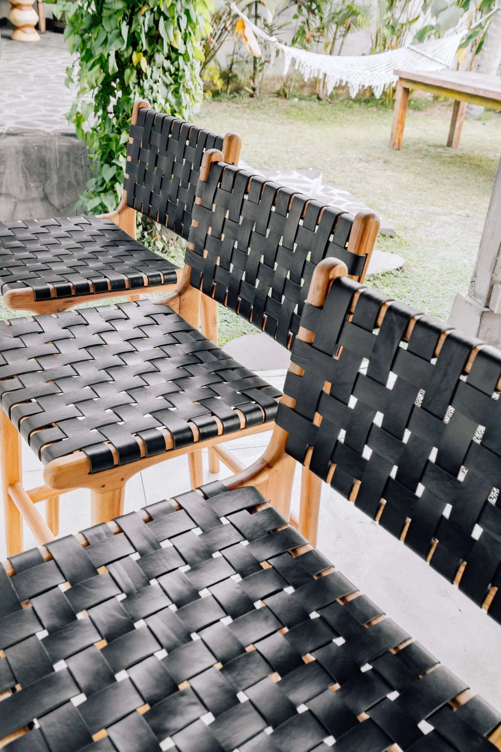Handmade woven black leather and wood chairs by Kayu Living in an outdoor setting