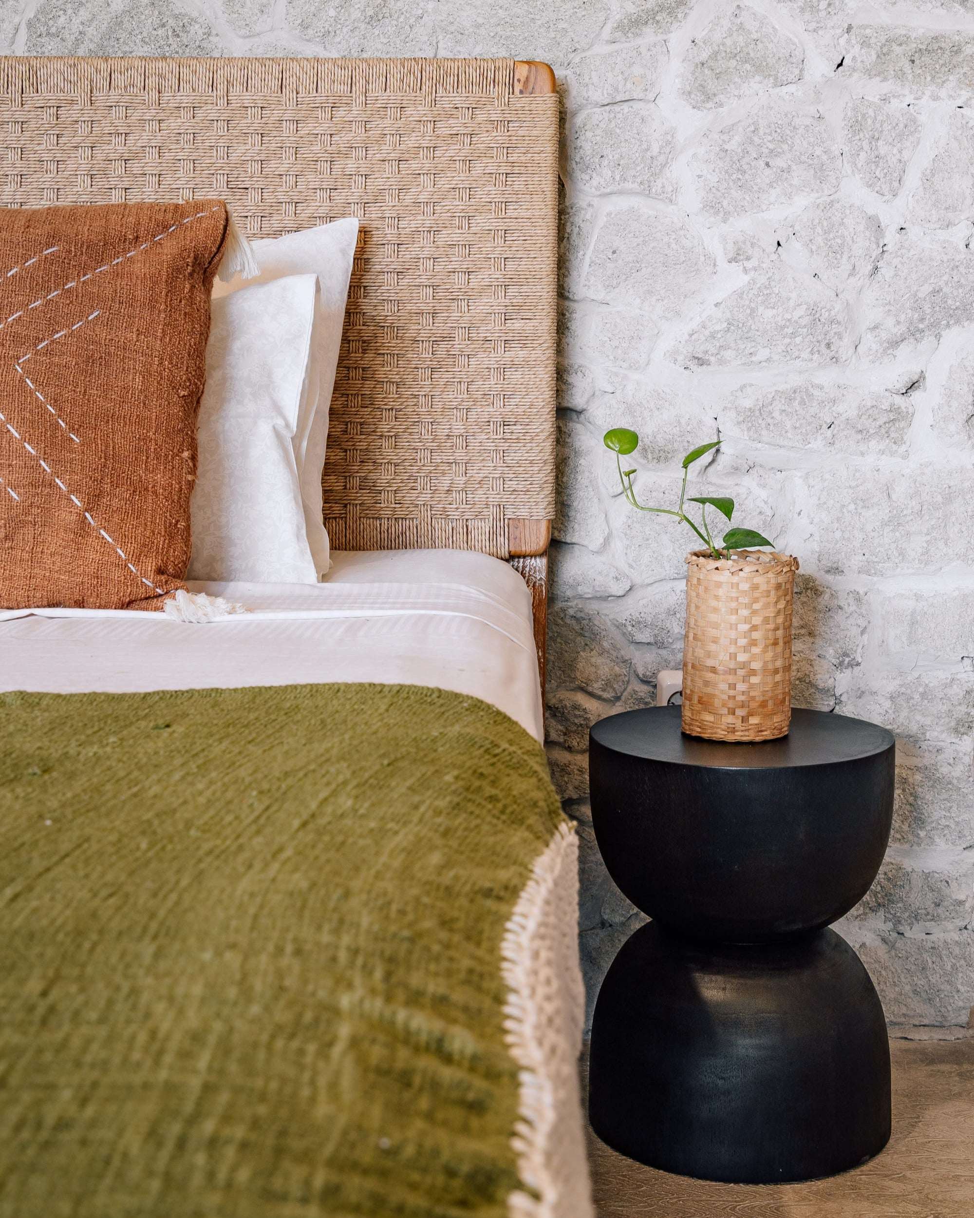 Handcrafted rattan headboard bed with green throw, modern black side table, stone wall, Kayu Living