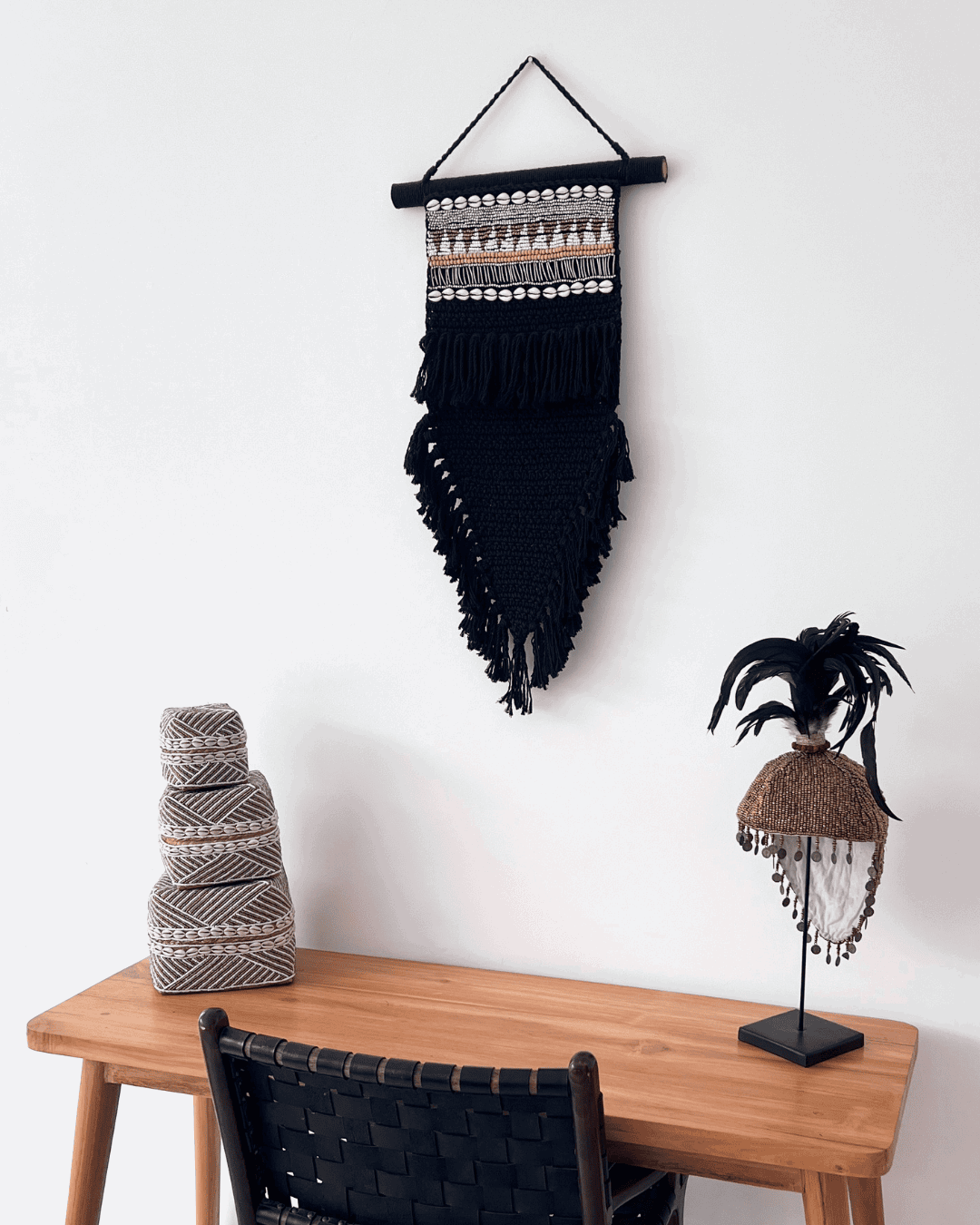 Decorative wall hanging with fringe and beads above a wooden table with decorative items.