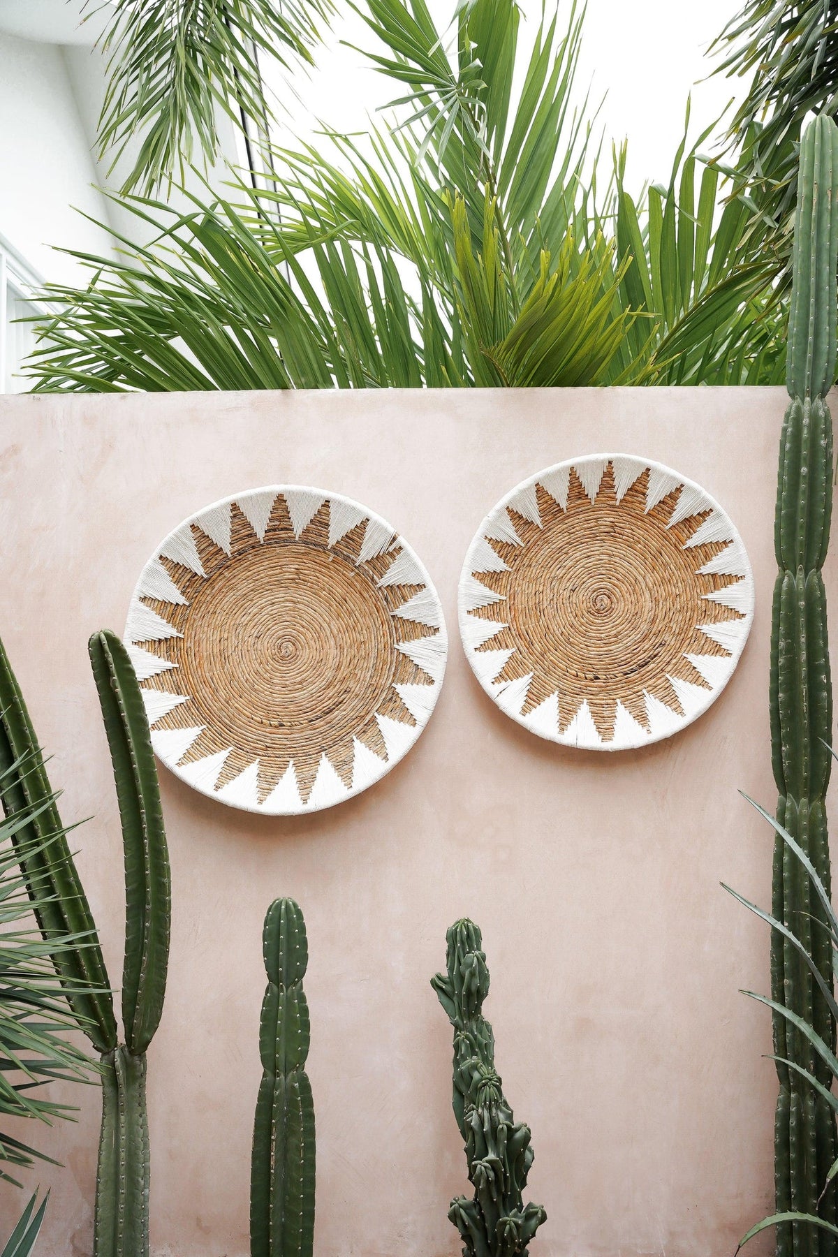 Two Kayu Living handcrafted bamboo star plates in white and brown, displayed as wall art on a pink outdoor wall.