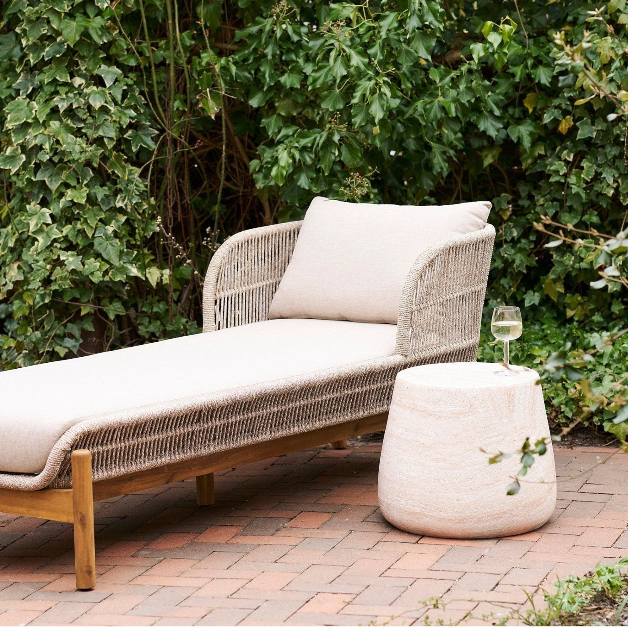 Kayu Living Bonn side table in natural fiberclay with a stone-like finish next to a wicker outdoor lounge chair.