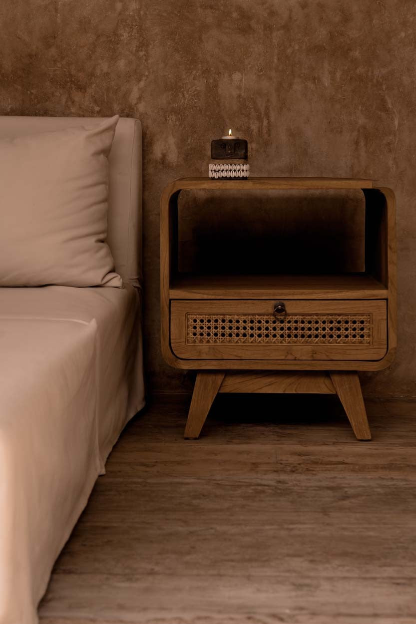 Kayu Living The Breeze nightstand in teak wood with a handwoven rattan drawer and open shelf in a bedroom setting.