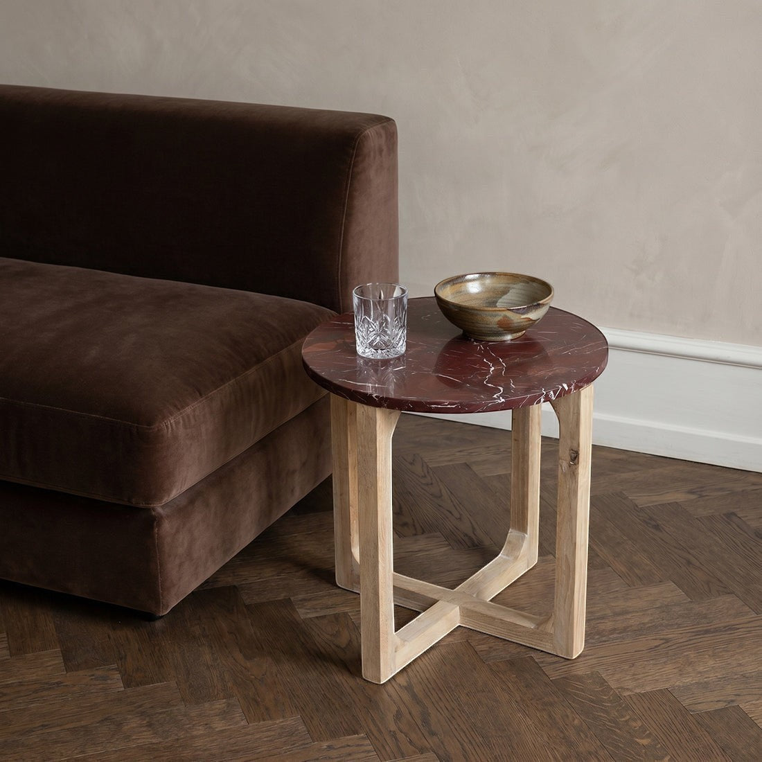 Kayu Living burgundy marble side table with white veins and a light mango wood cross-leg base next to a brown sofa.