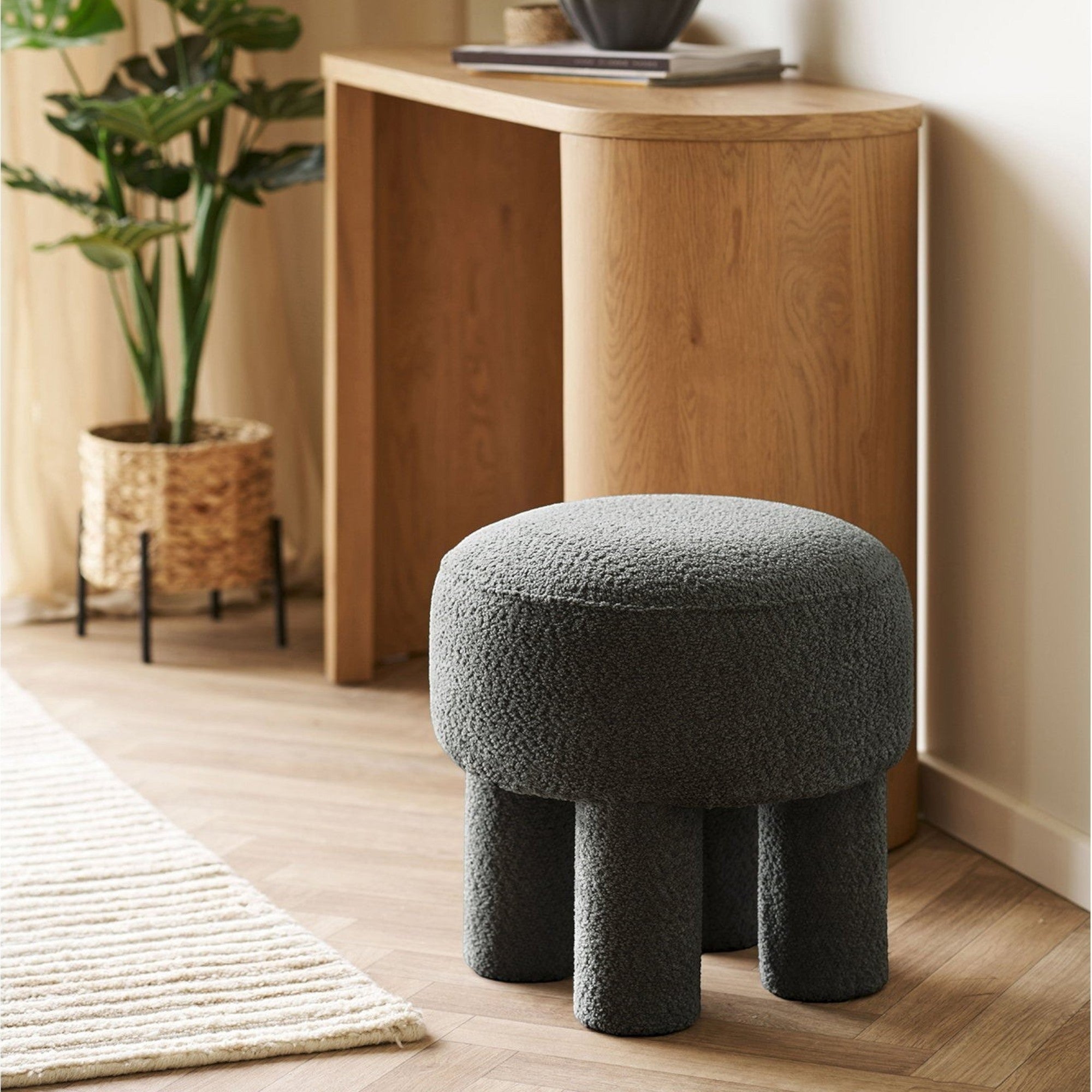 Kayu Living charcoal round pouf upholstered in textured polyester with four short legs, perfect as accent seating or footrest.