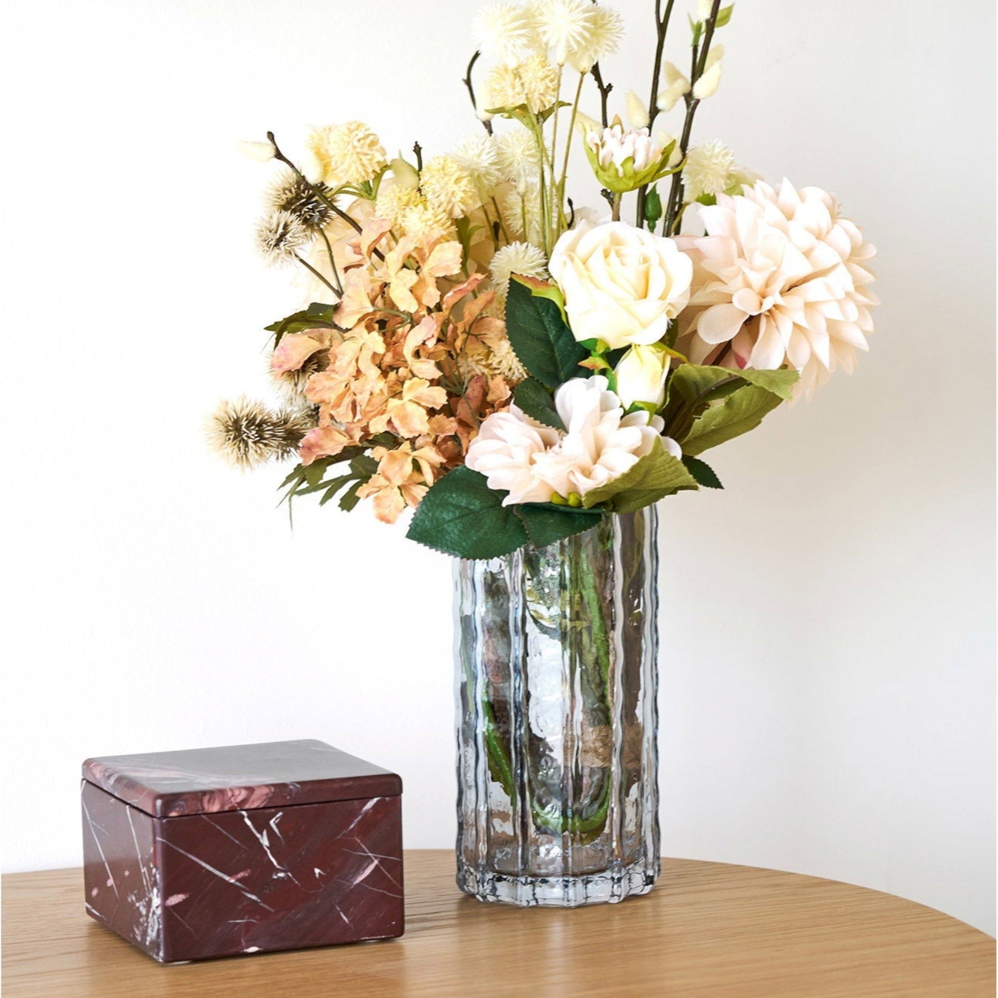Kayu Living chestnut-red marble jar with a square lid, displayed on a wooden table next to a glass flower vase.