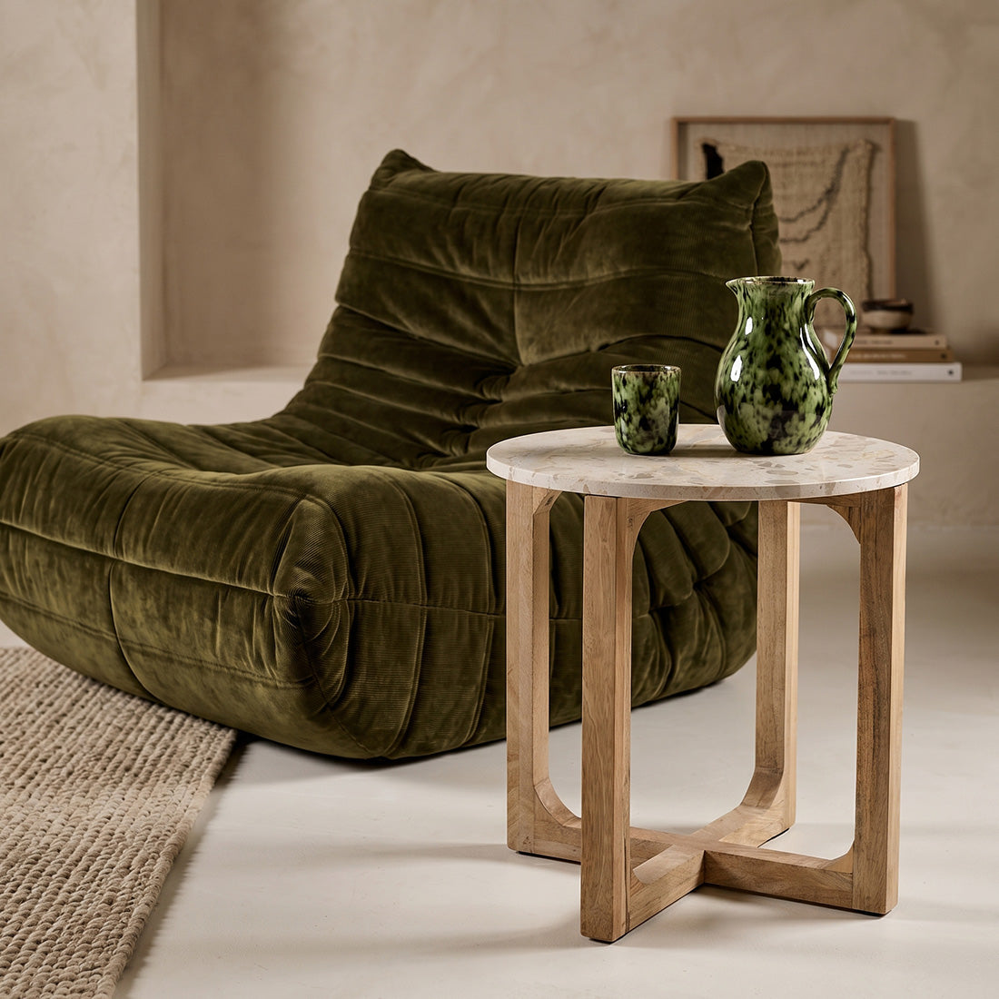 Kayu Living cream marble side table with a round top and open mango wood base next to a green velvet lounge chair